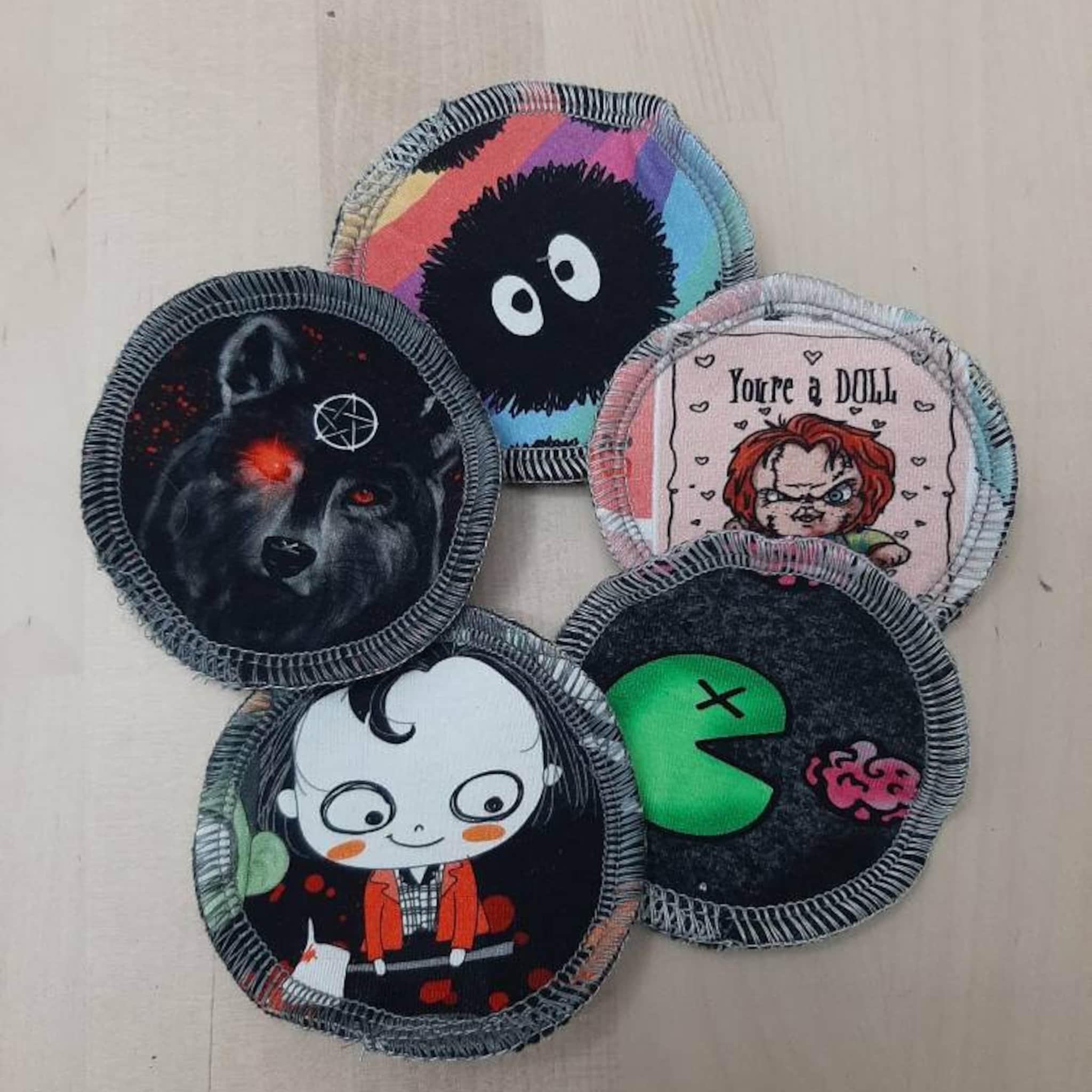Round fabric patches with various illustrations, black stitched edges, and colorful designs including wolf and cartoon characters