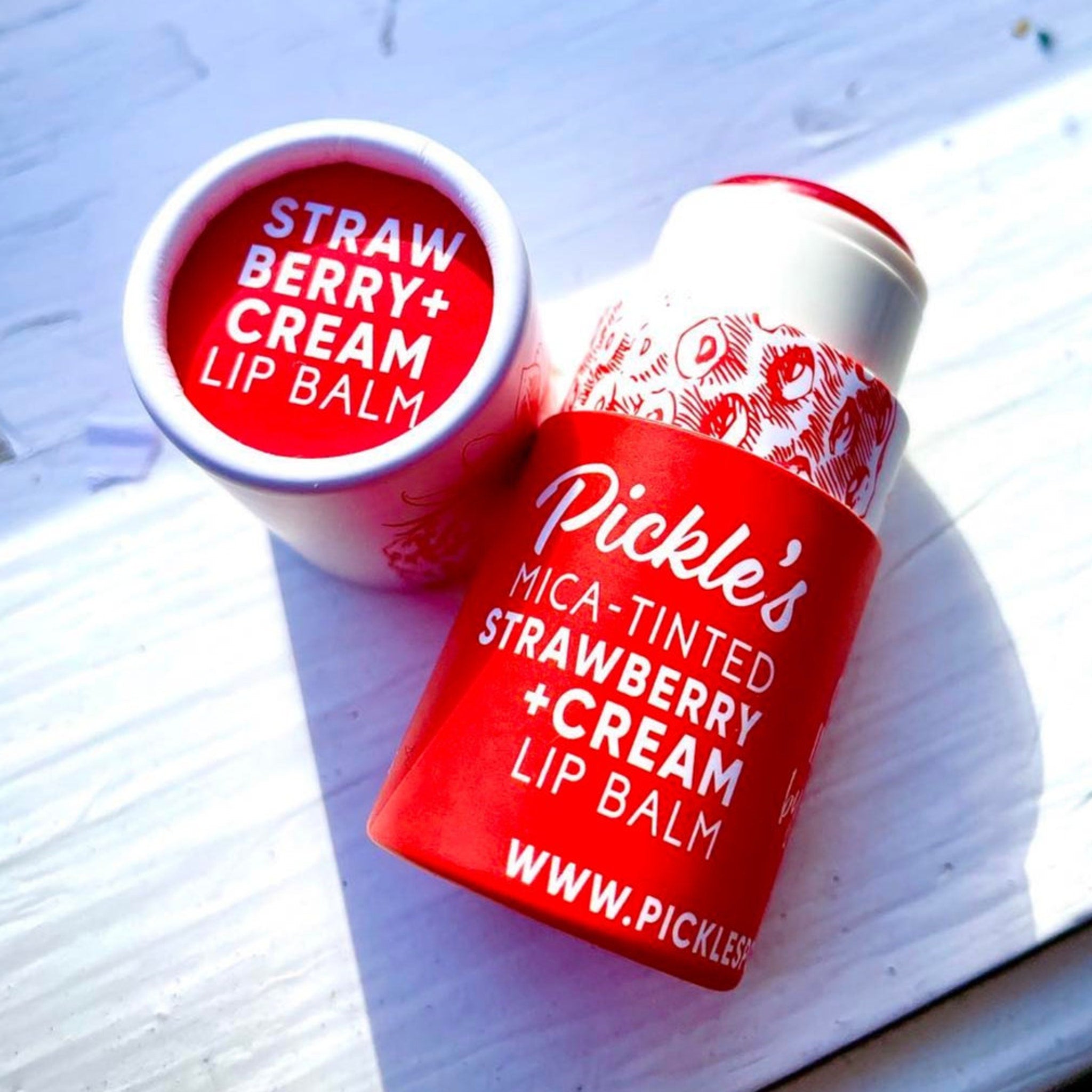 Lip balm tubes, red and white with strawberry pattern, Pickle's brand visible, on white surface
