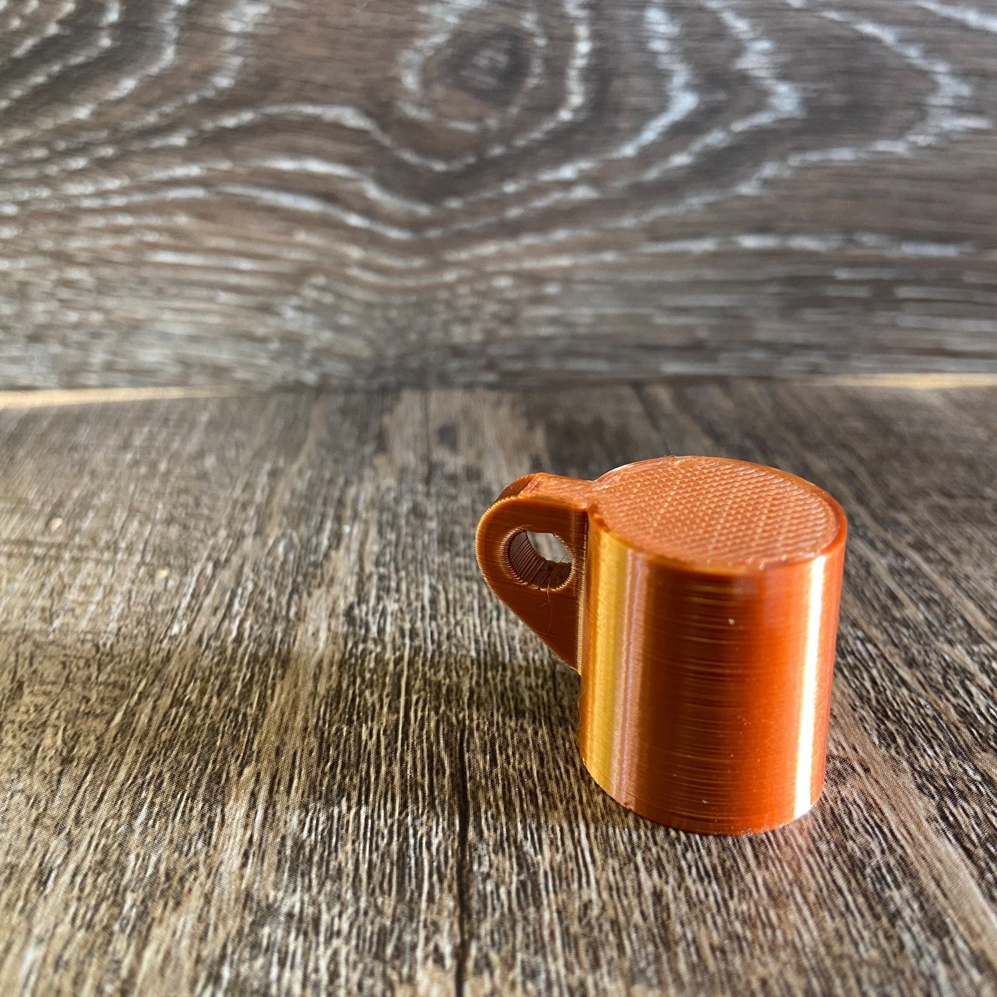 Orange 3D printed cylinder with handle, textured surface, on wood background