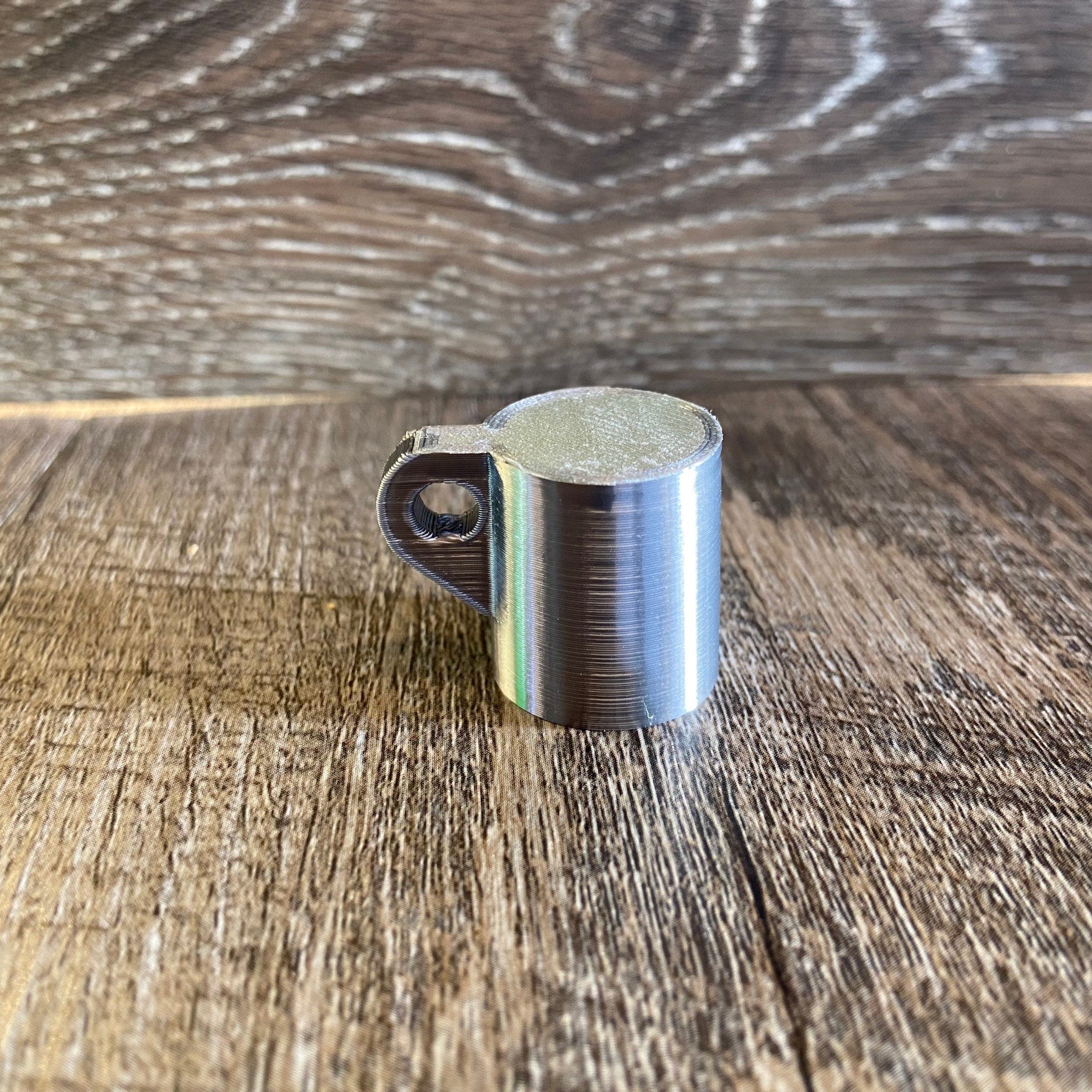 Metal cup with silver color, cylindrical shape, and handle detail on wooden surface