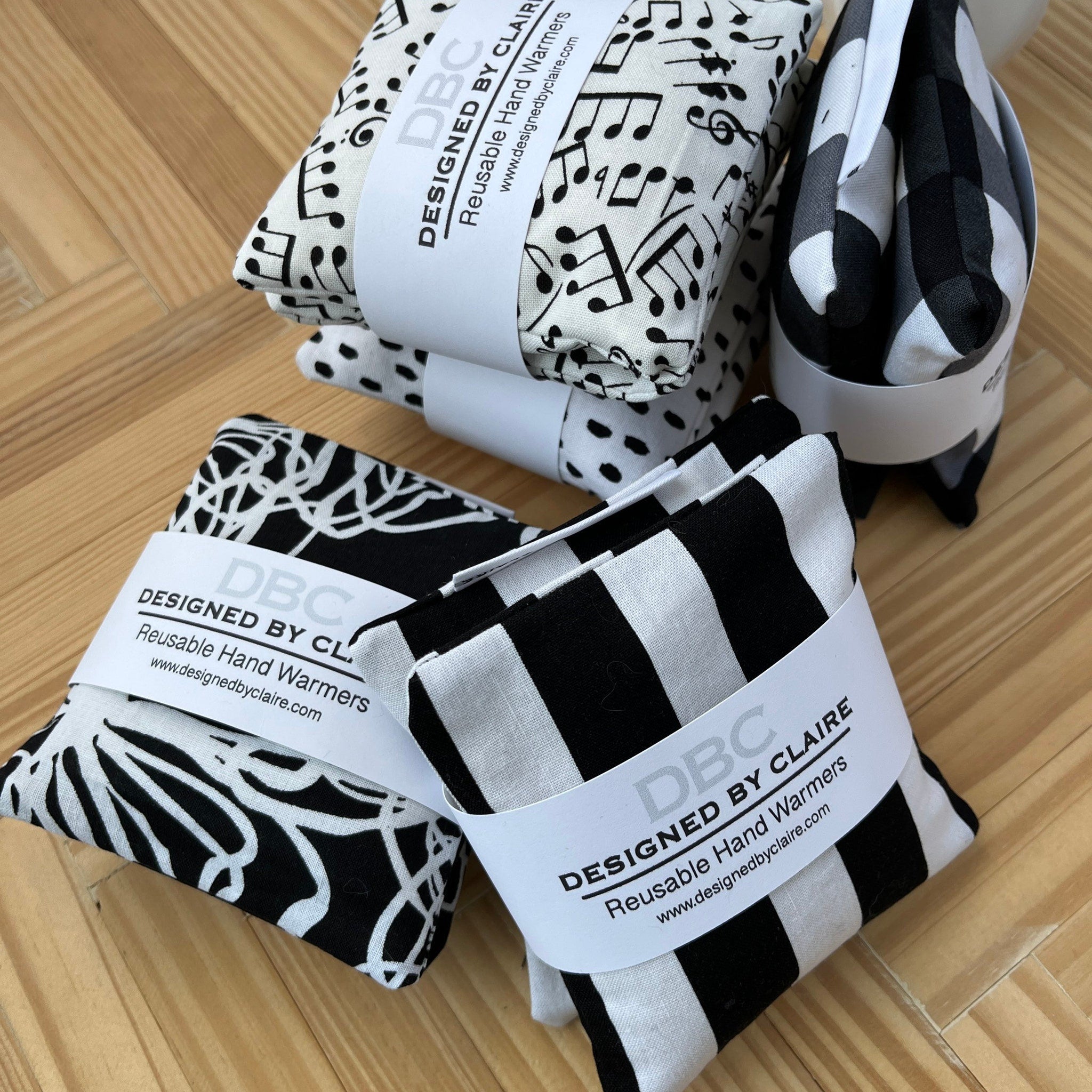 Reusable hand warmers, black and white patterns, DBC brand visible, stacked on wood surface