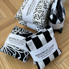 Reusable hand warmers, black and white patterns, DBC brand visible, stacked on wood surface