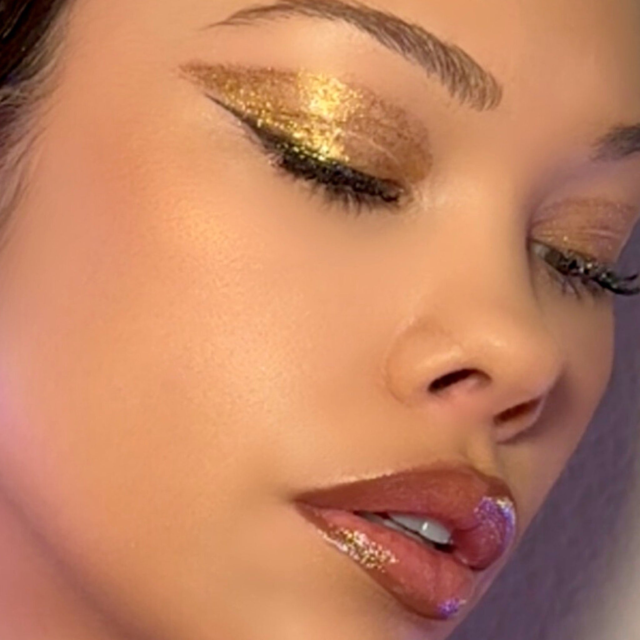 Hand applying gold glitter gel eyeshadow to eyelid with fingertip for shimmering makeup look