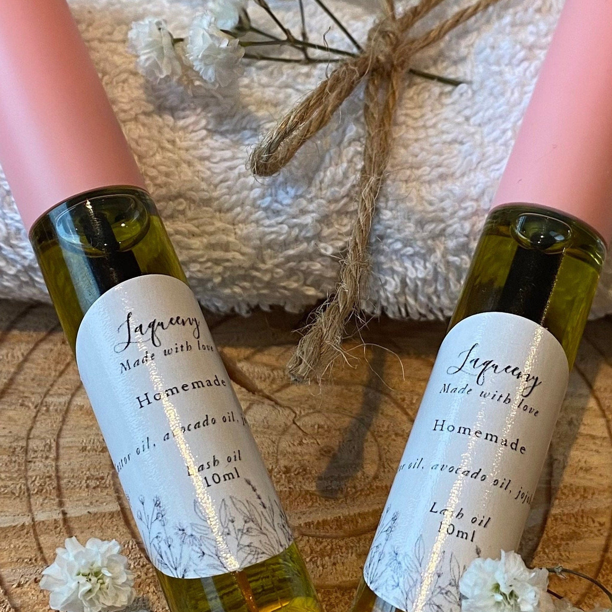 Lash oil bottles with pink cap, Laqueeny label, and floral design, on wood surface
