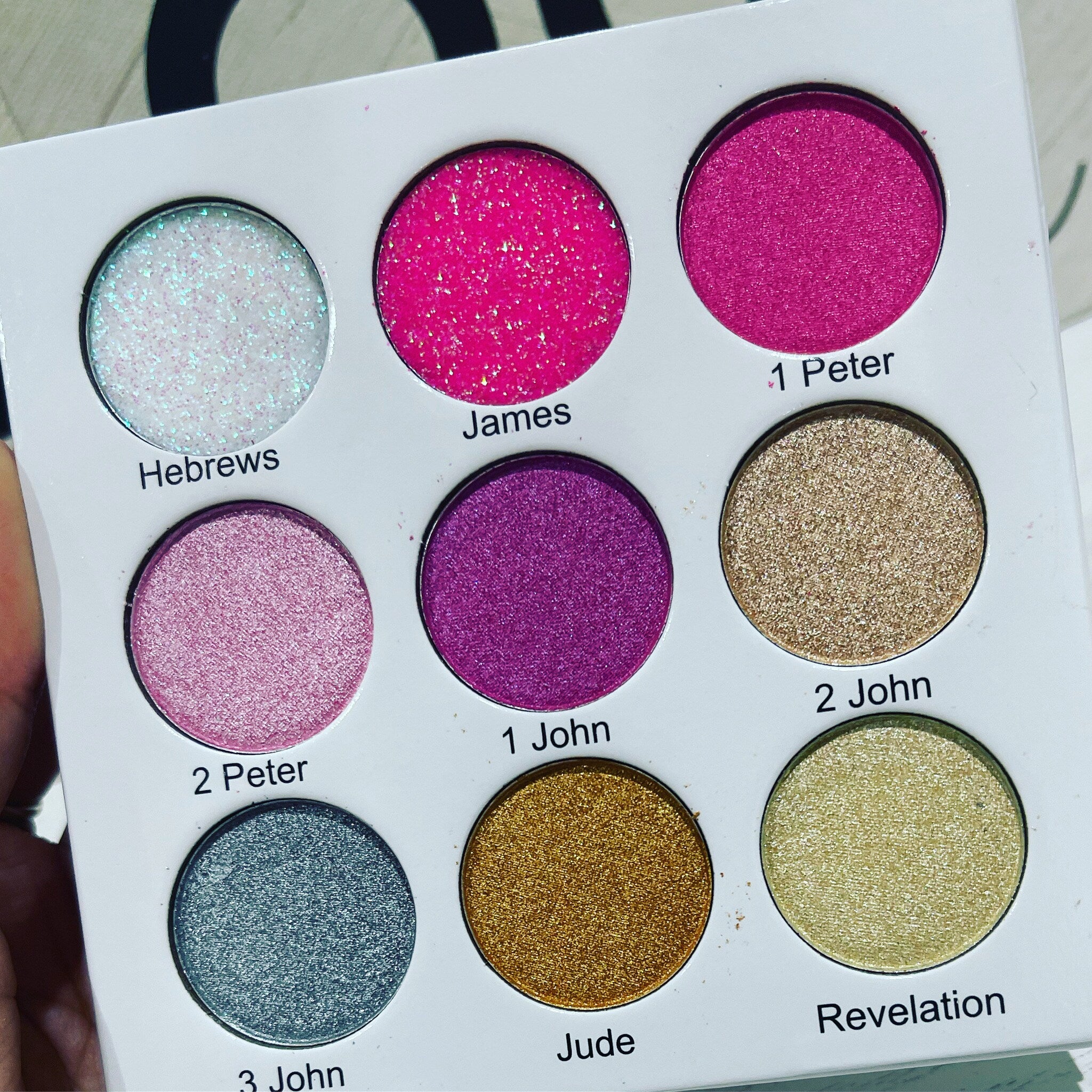 Eyeshadow palette with various colors and glitter finish, labeled with text on white background