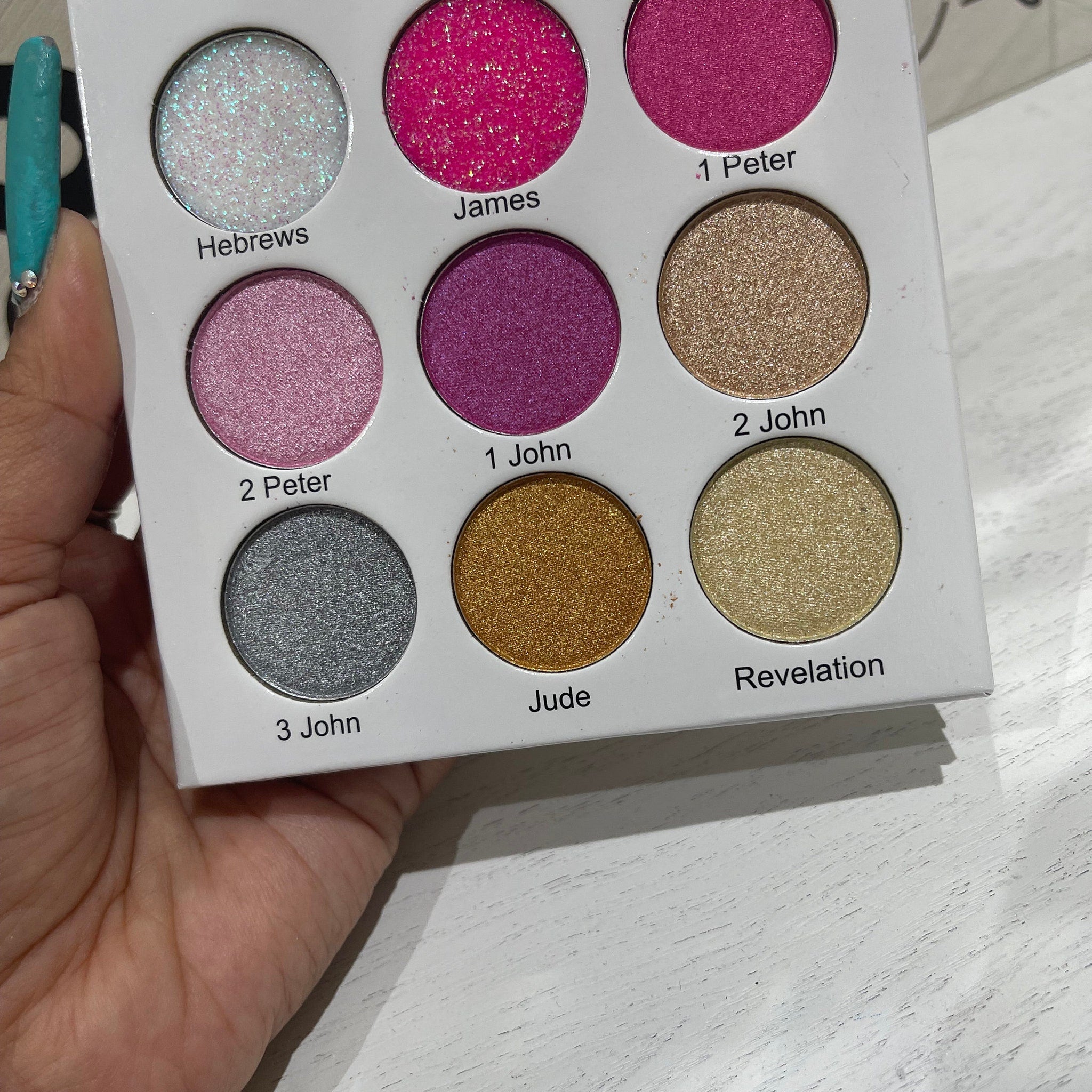 Eyeshadow palette with multiple colors, including pink, gold, and silver shimmer shades, in a white compact held by a hand