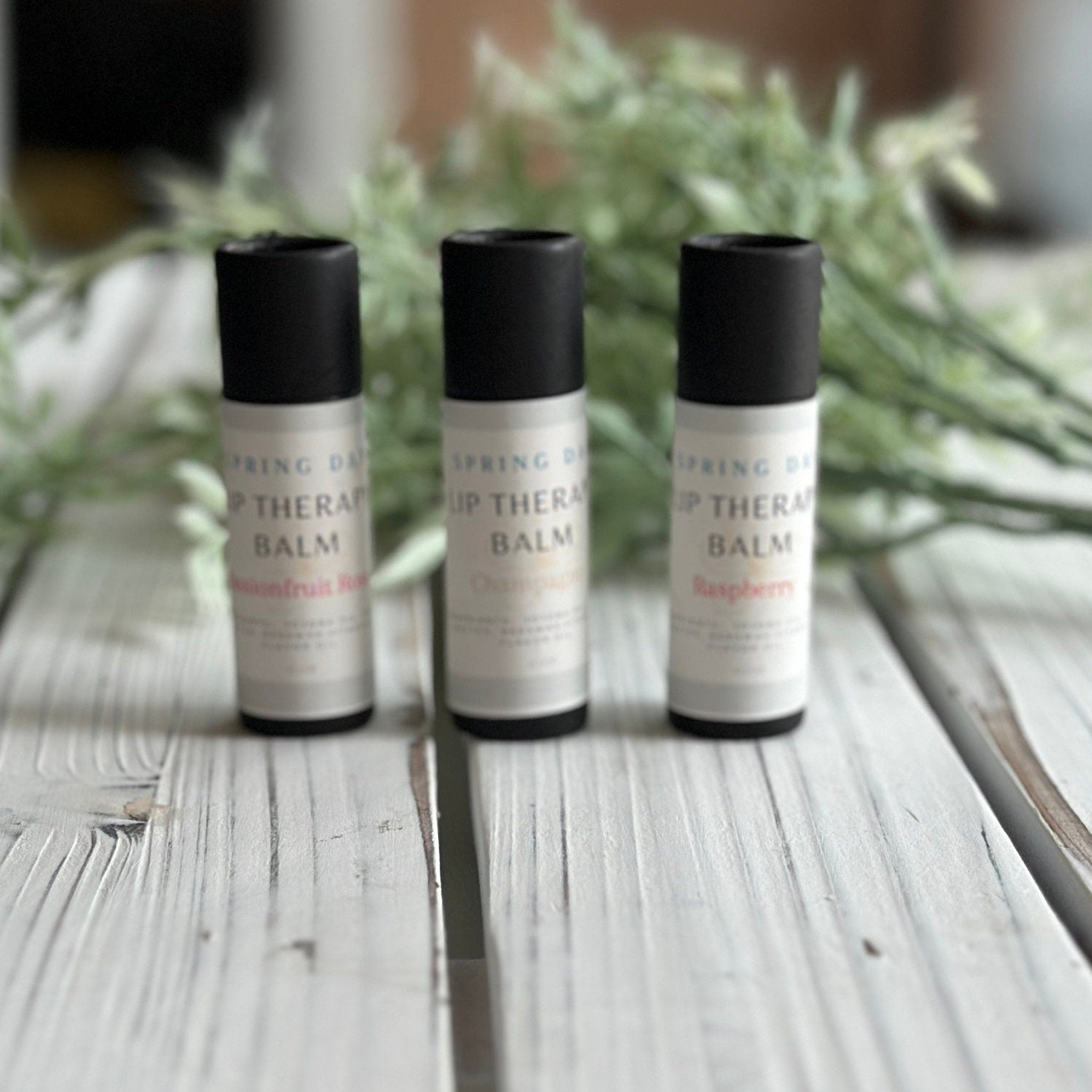 Lip balm tubes with black caps and white labels, Springday Soapery branding visible, on wood surface