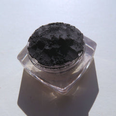 Black powder in clear plastic container, on white surface with shadow