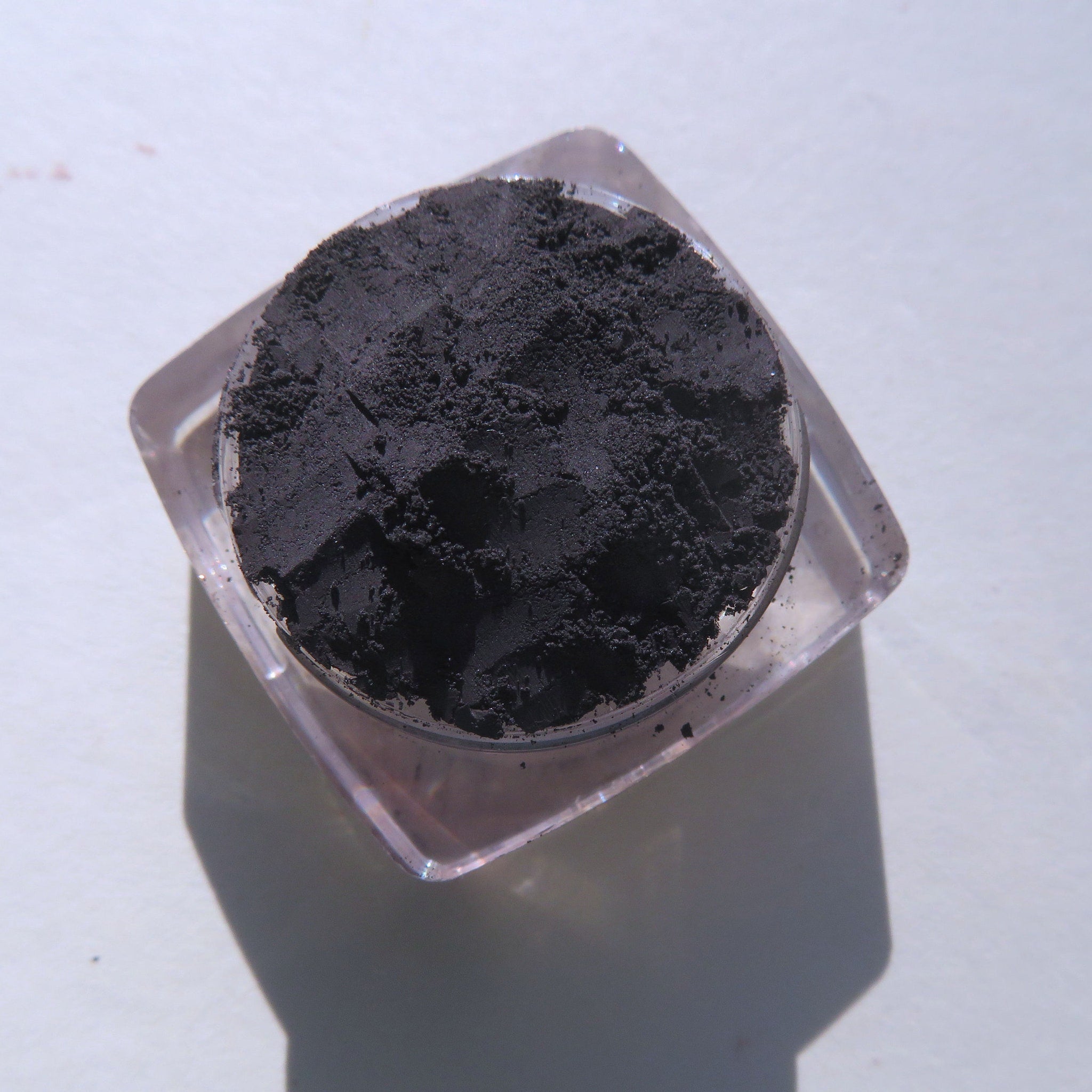 Black powder in clear plastic container, textured powder, overhead view