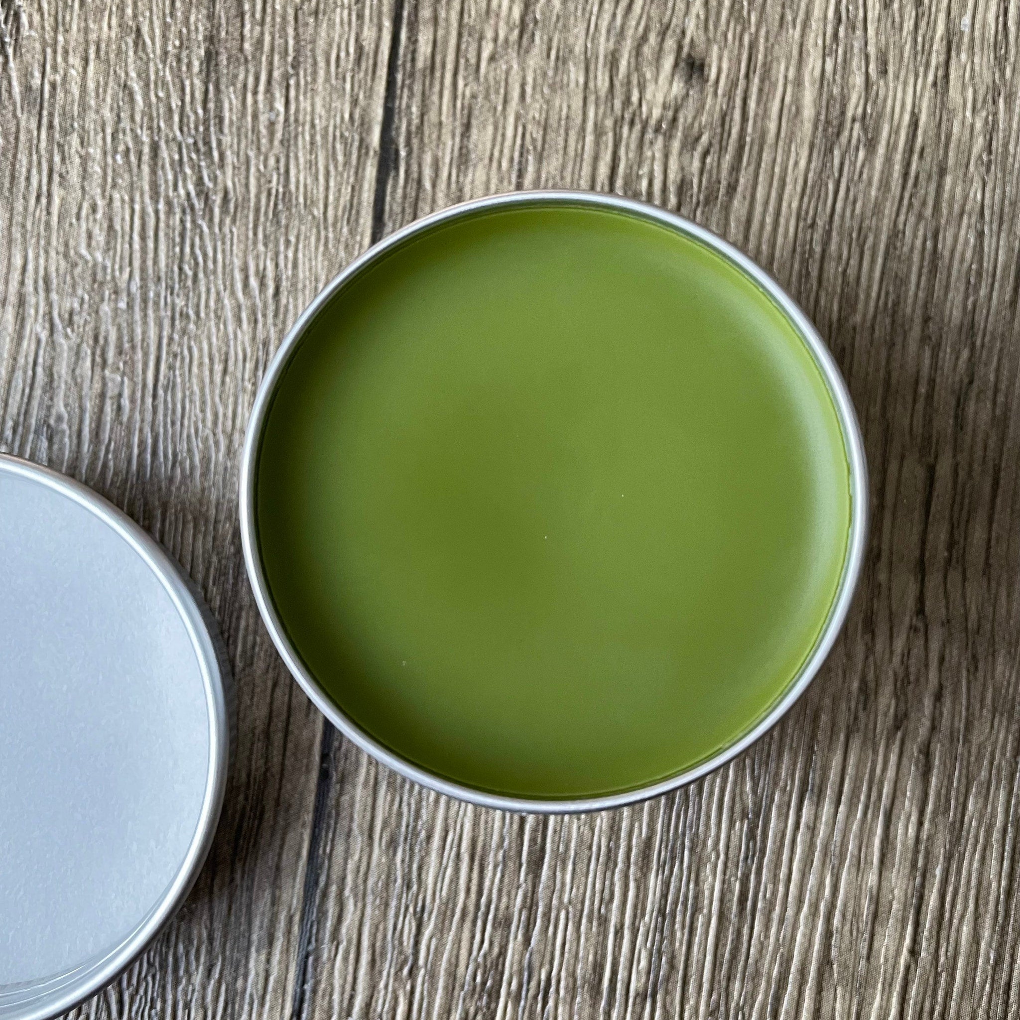 Green product in silver tin, on wood grain surface, open lid visible