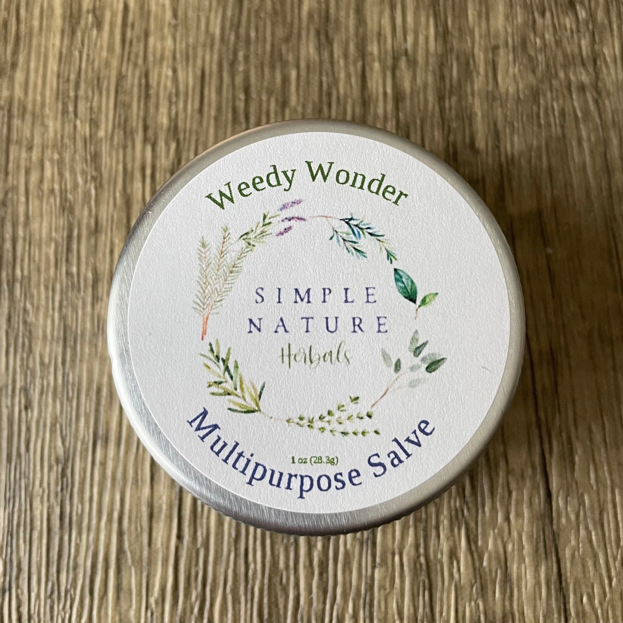Multipurpose salve tin with white label, green and blue text, and floral design on wood surface