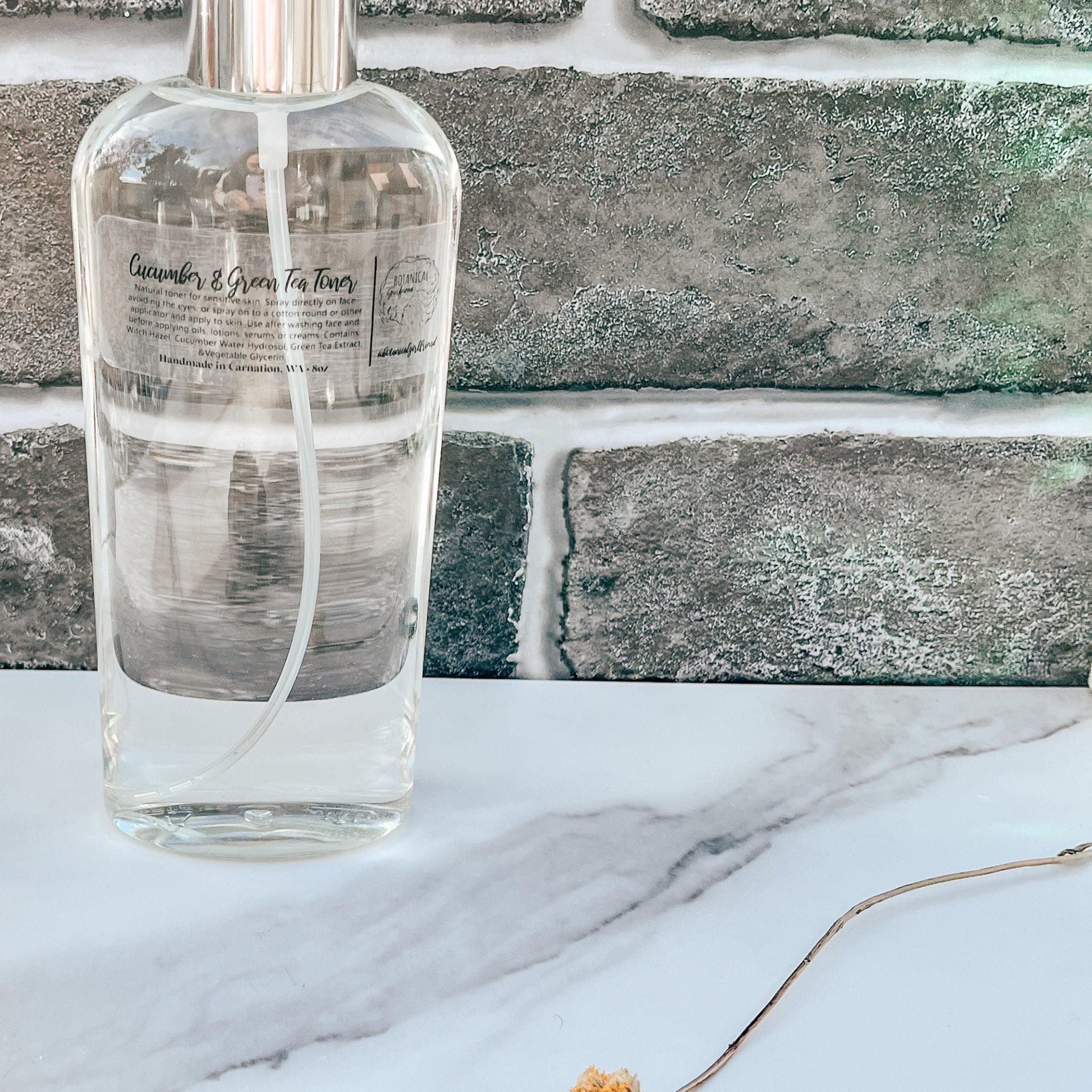 Toner bottle, clear glass with silver sprayer, Cucumber & Green Tea Toner label, on marble surface