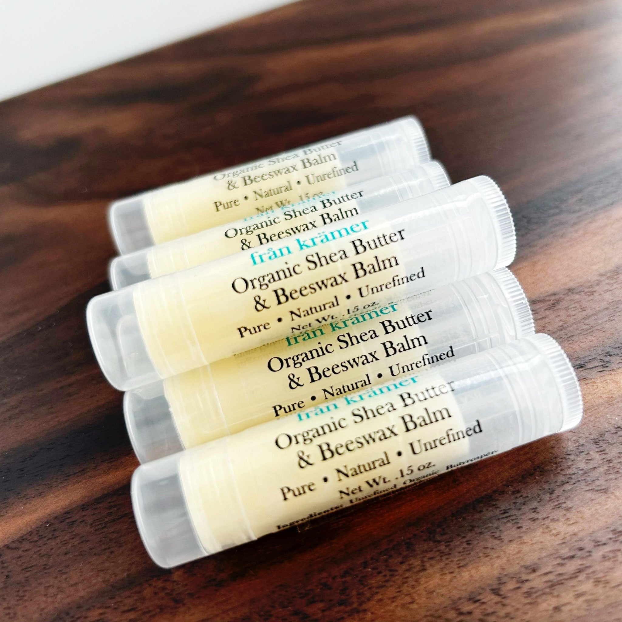 Lip balm tubes with white and clear plastic, yellow balm, and "från krämer" text on a wooden surface