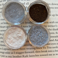 Eyeshadow powder in silver, brown, and pink shades, displayed in small clear jars