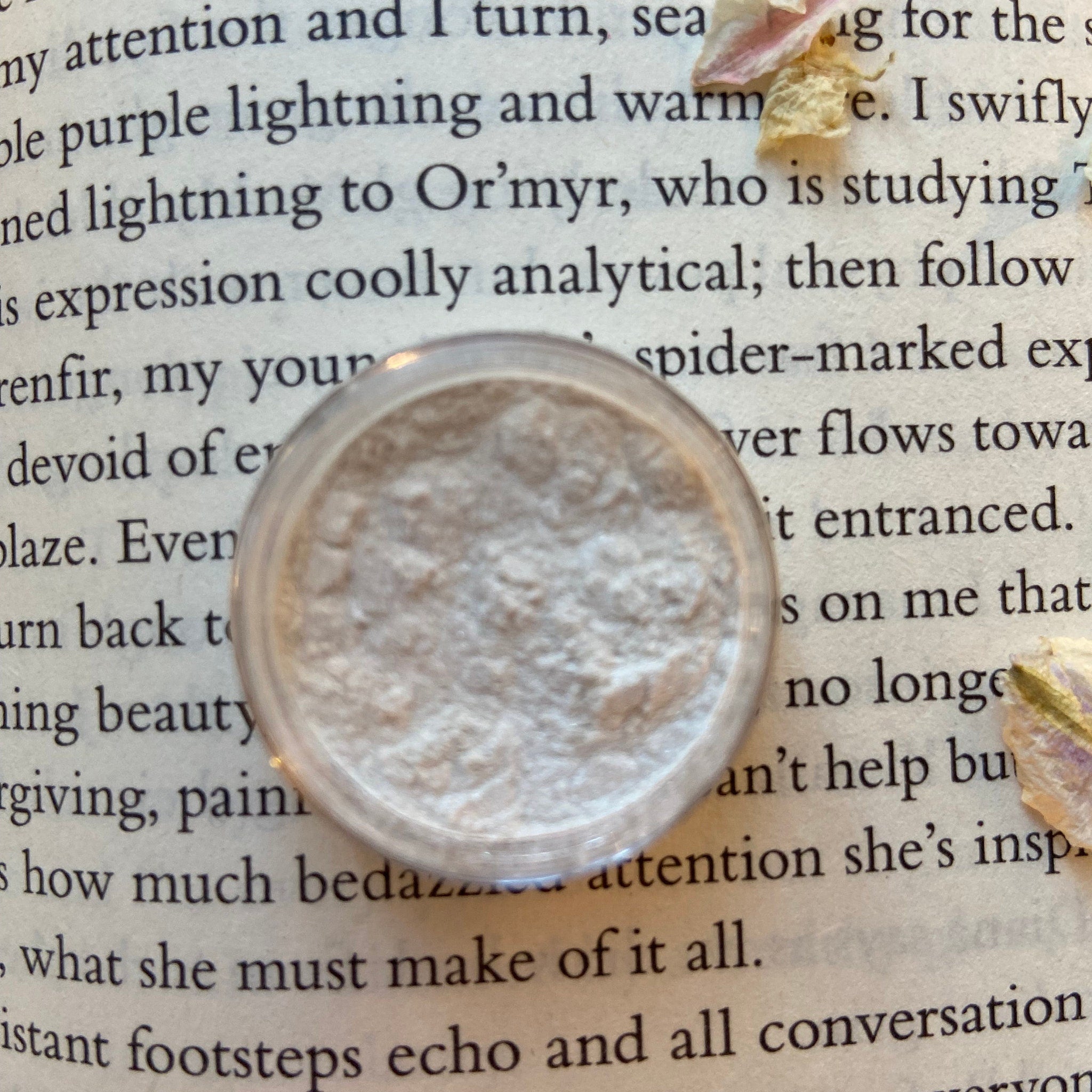 Powdered makeup, light beige powder, clear plastic container, on book page