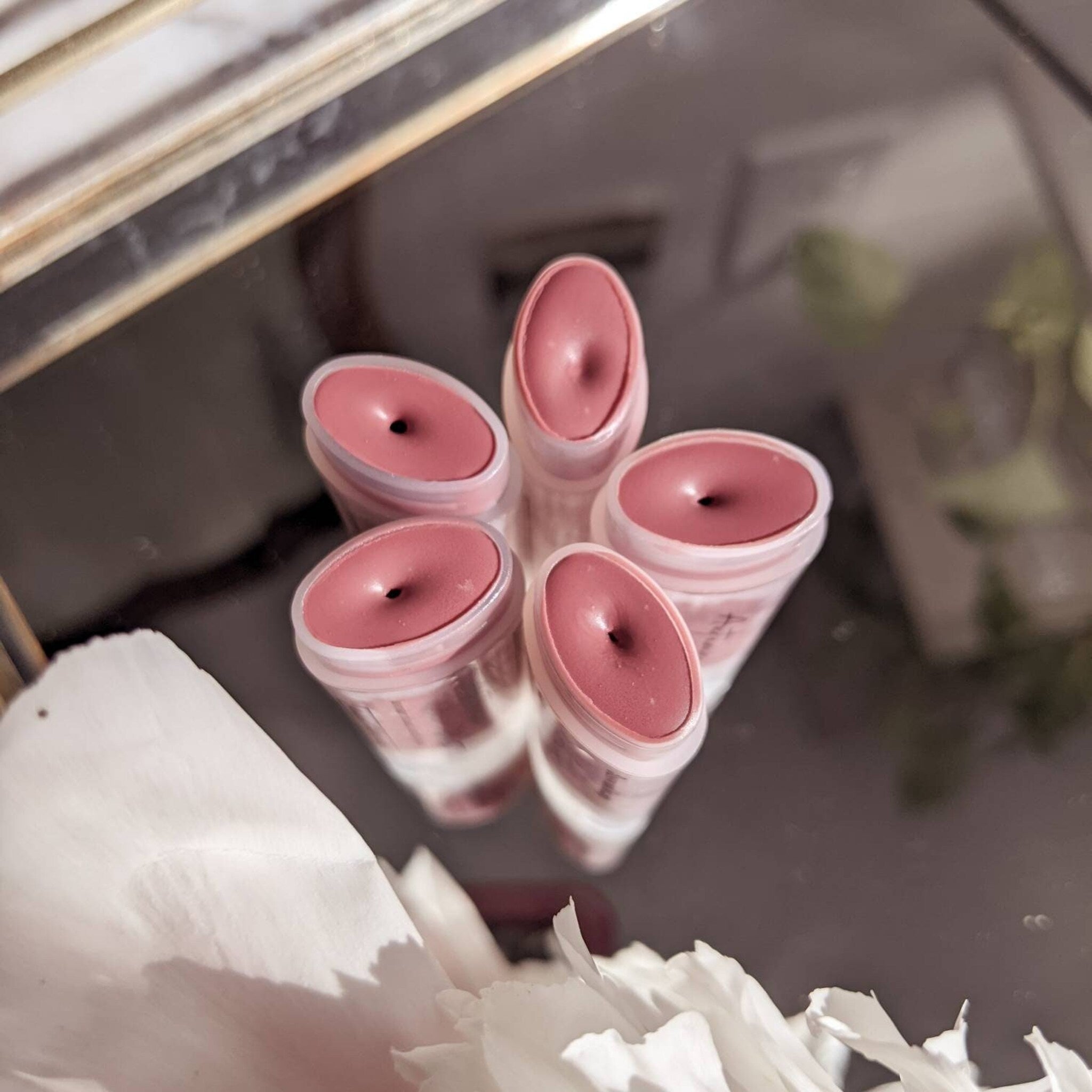 Lip balm tubes with pink color, plastic containers, and a reflective surface.
