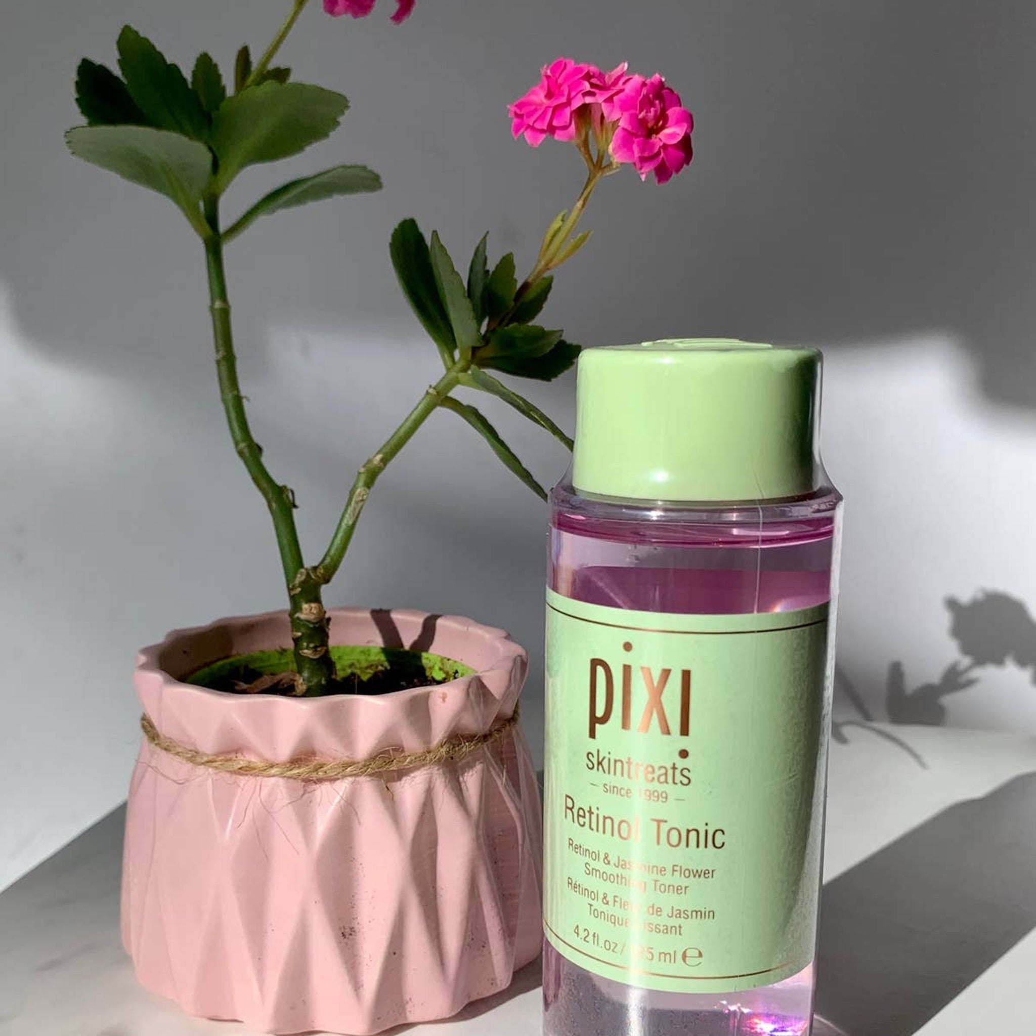 Retinol Tonic bottle with green cap and label, pink liquid, and plant in pink pot with rope trim