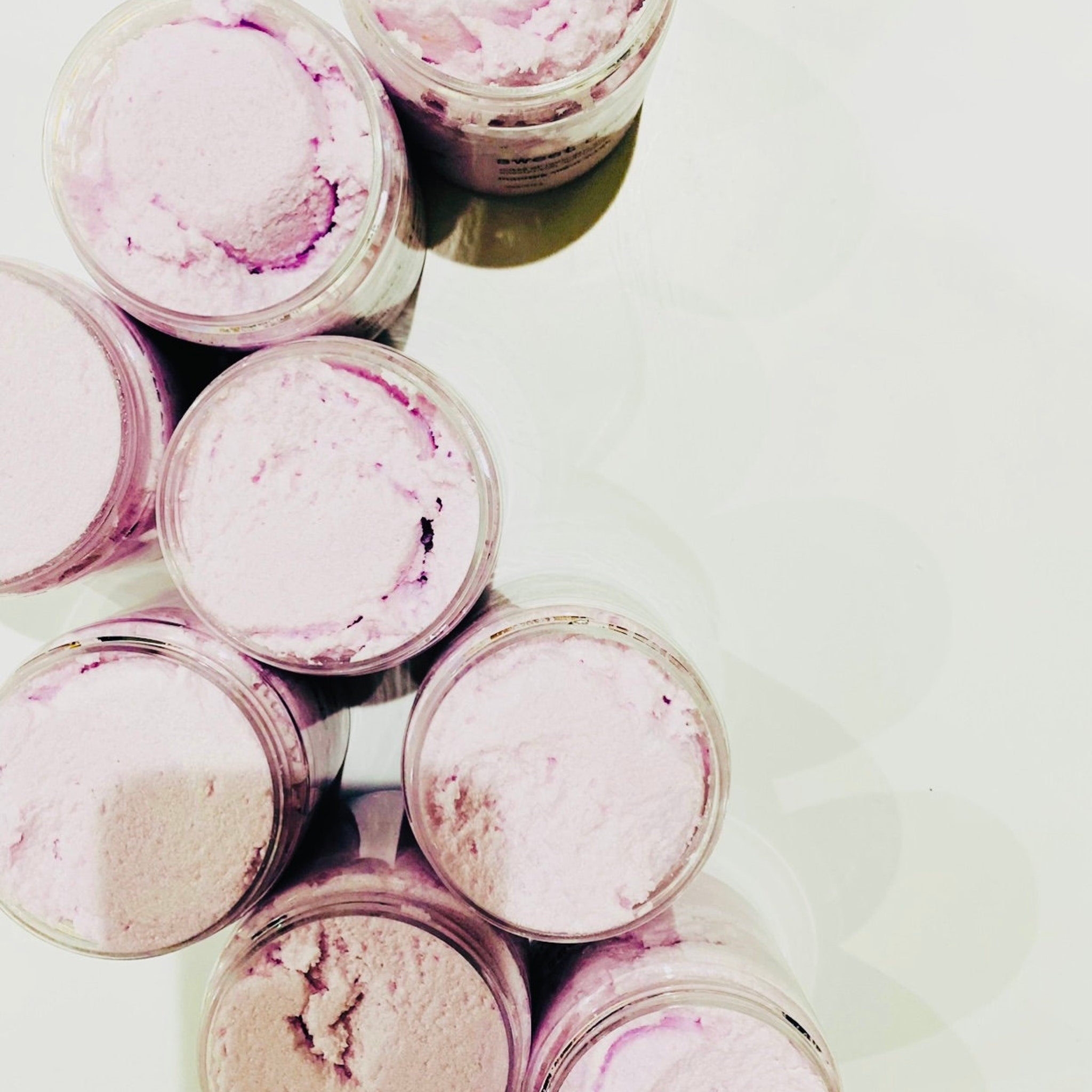 Whipped body butter in clear plastic jars, light pink and purple swirls, top view