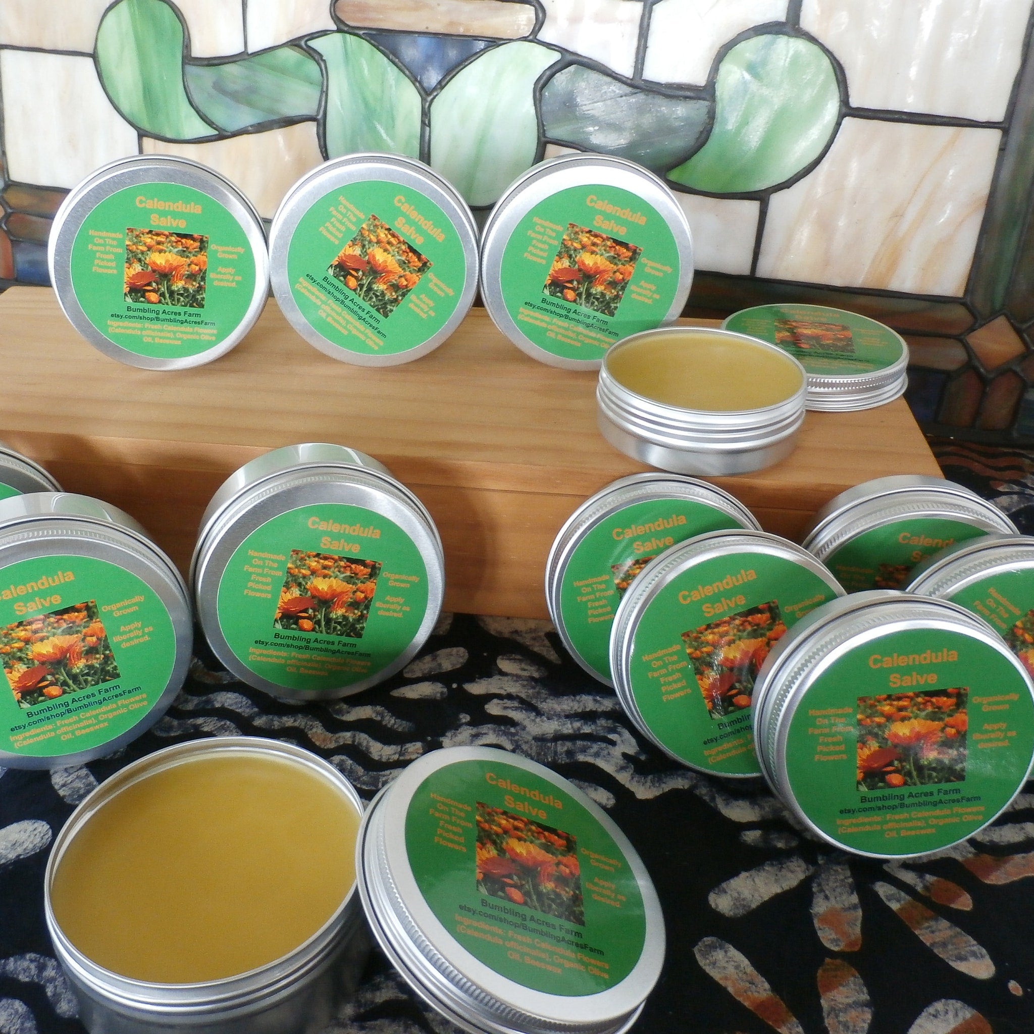 Calendula salve in silver tins with green labels, yellow balm visible, Bumbling Acres Farm text