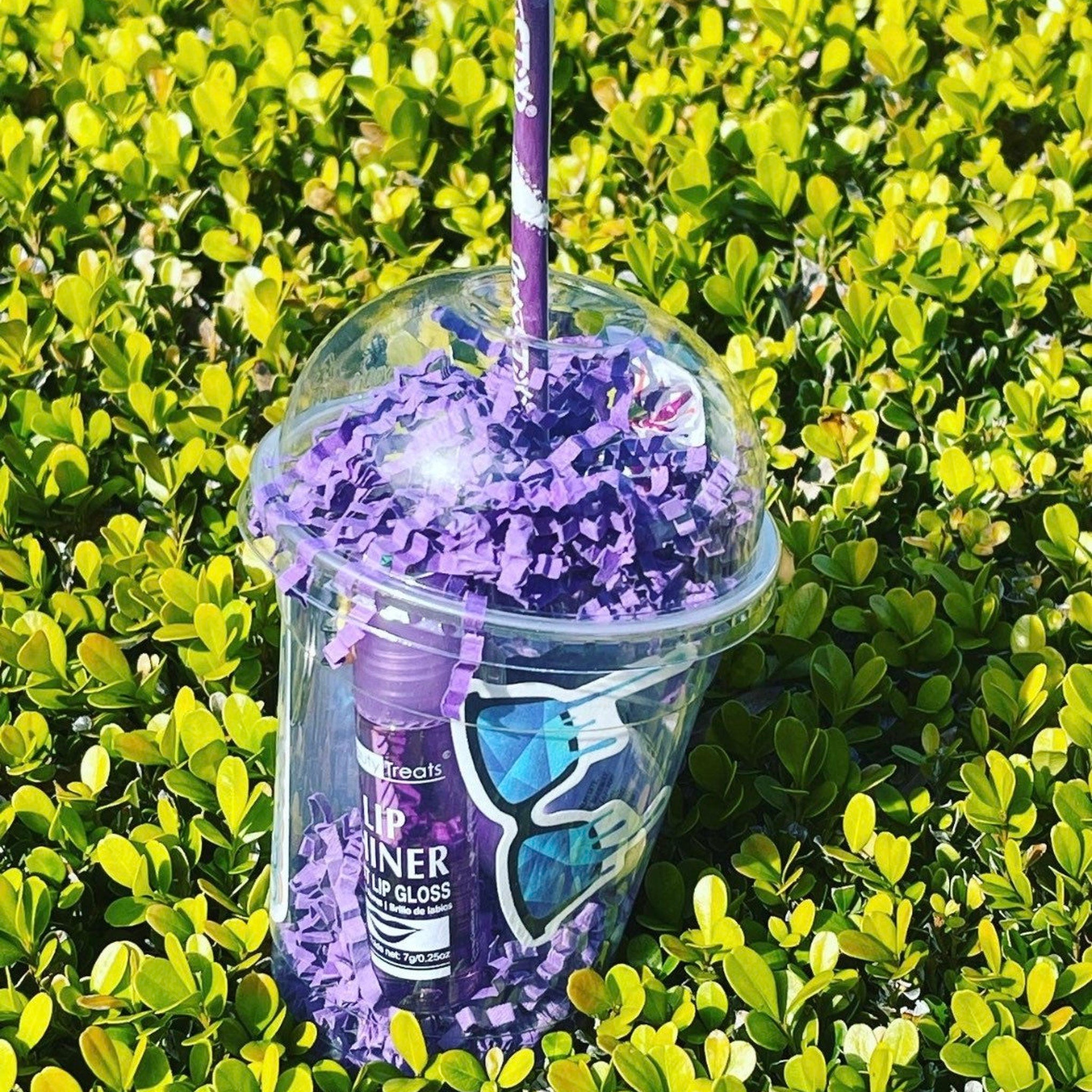Lip gloss gift set with purple packaging, clear cup, and purple confetti inside a green bush