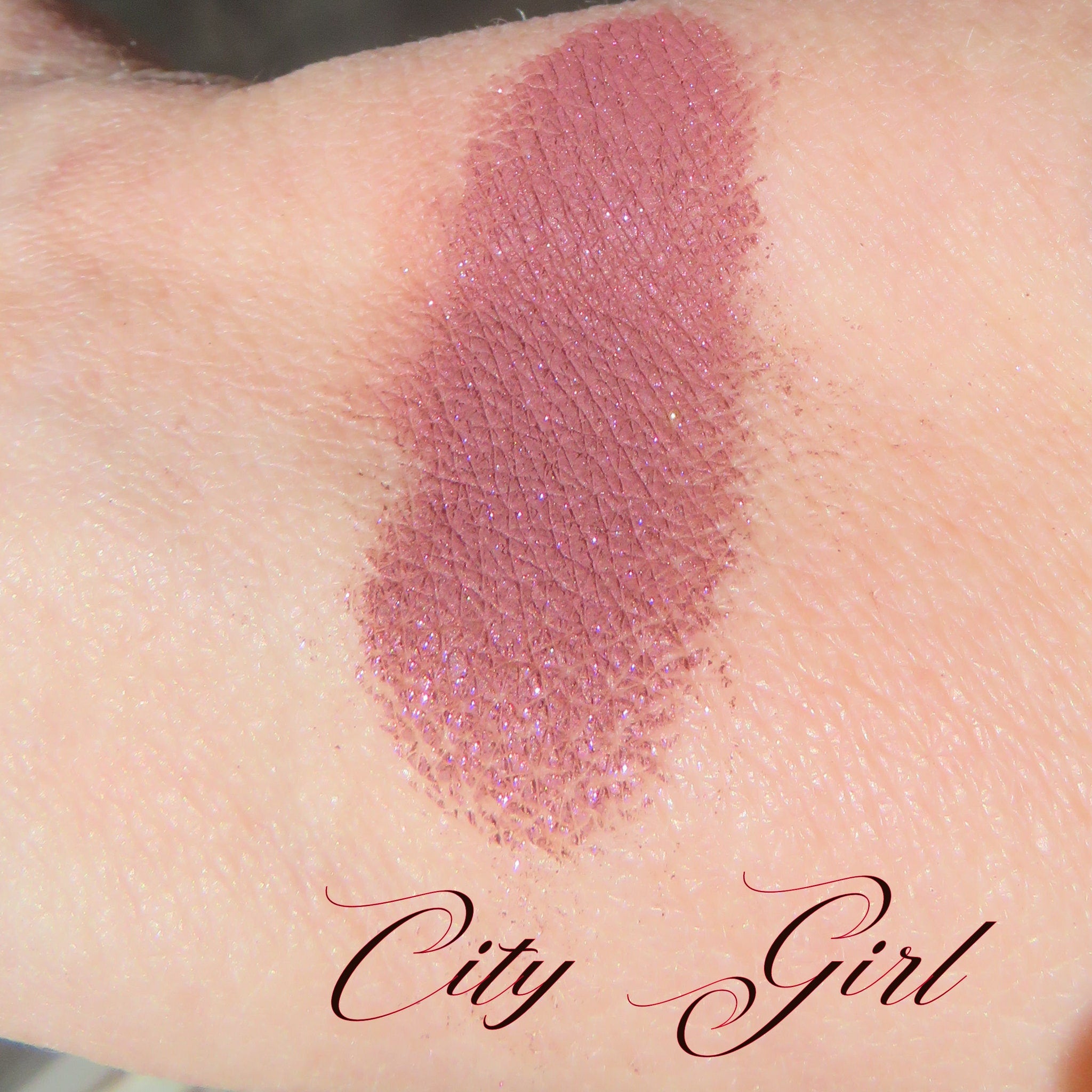 Close-up of loose dark mauve eye shadow with pink sheen, showcasing vegan mineral pigment texture in jar