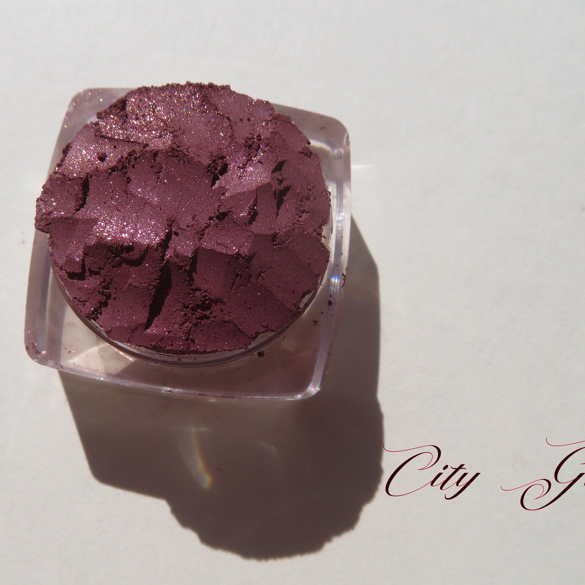 Loose vegan mineral eye shadow in dark mauve with shimmering pink sheen, cruelty-free, displayed in open jar.