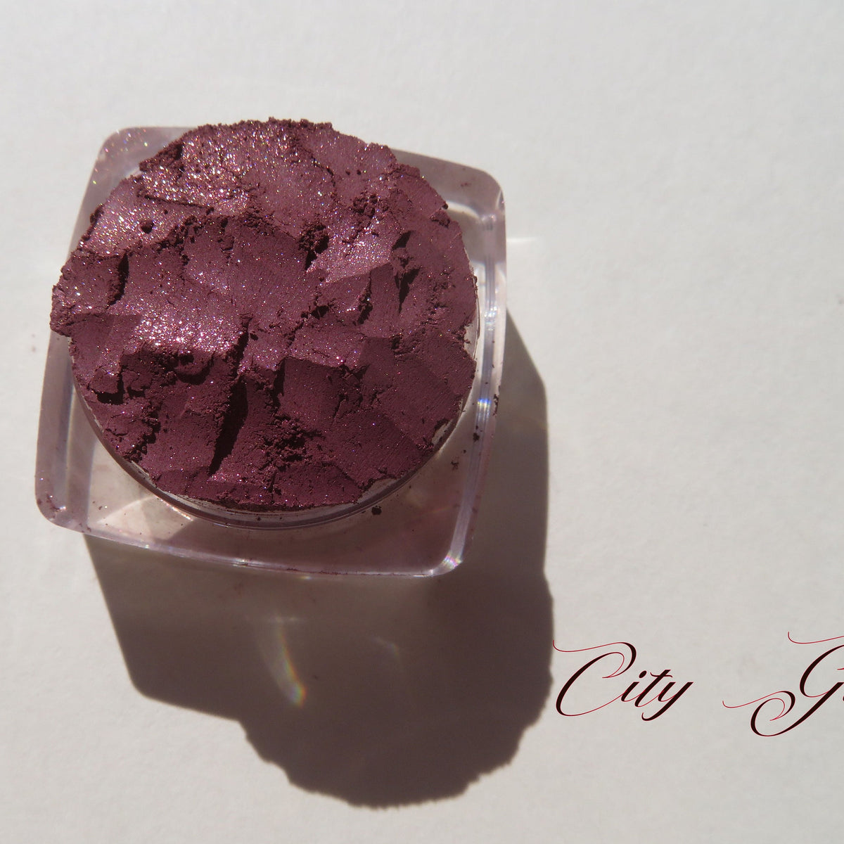 Loose vegan mineral eye shadow in dark mauve with shimmering pink sheen, cruelty-free, displayed in open jar.