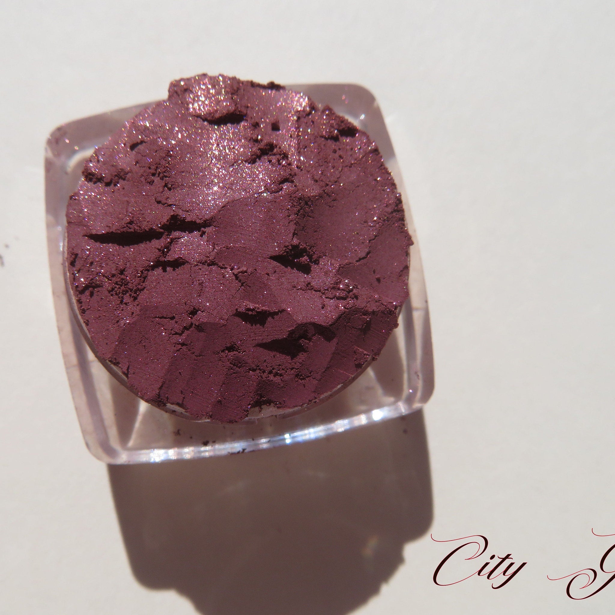 Side view of loose vegan mineral eye shadow in dark mauve with pink sheen, showcasing fine pigment texture