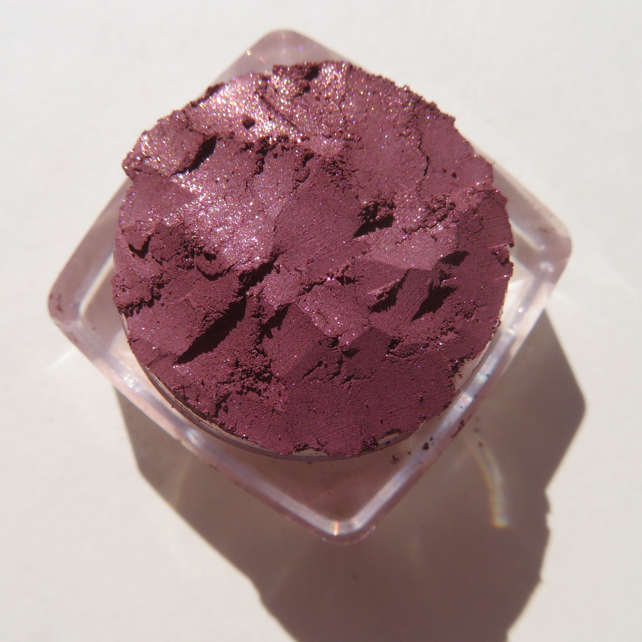 Open jar of vegan loose mineral eye shadow in dark mauve with pink sheen, showcasing fine pigment texture.