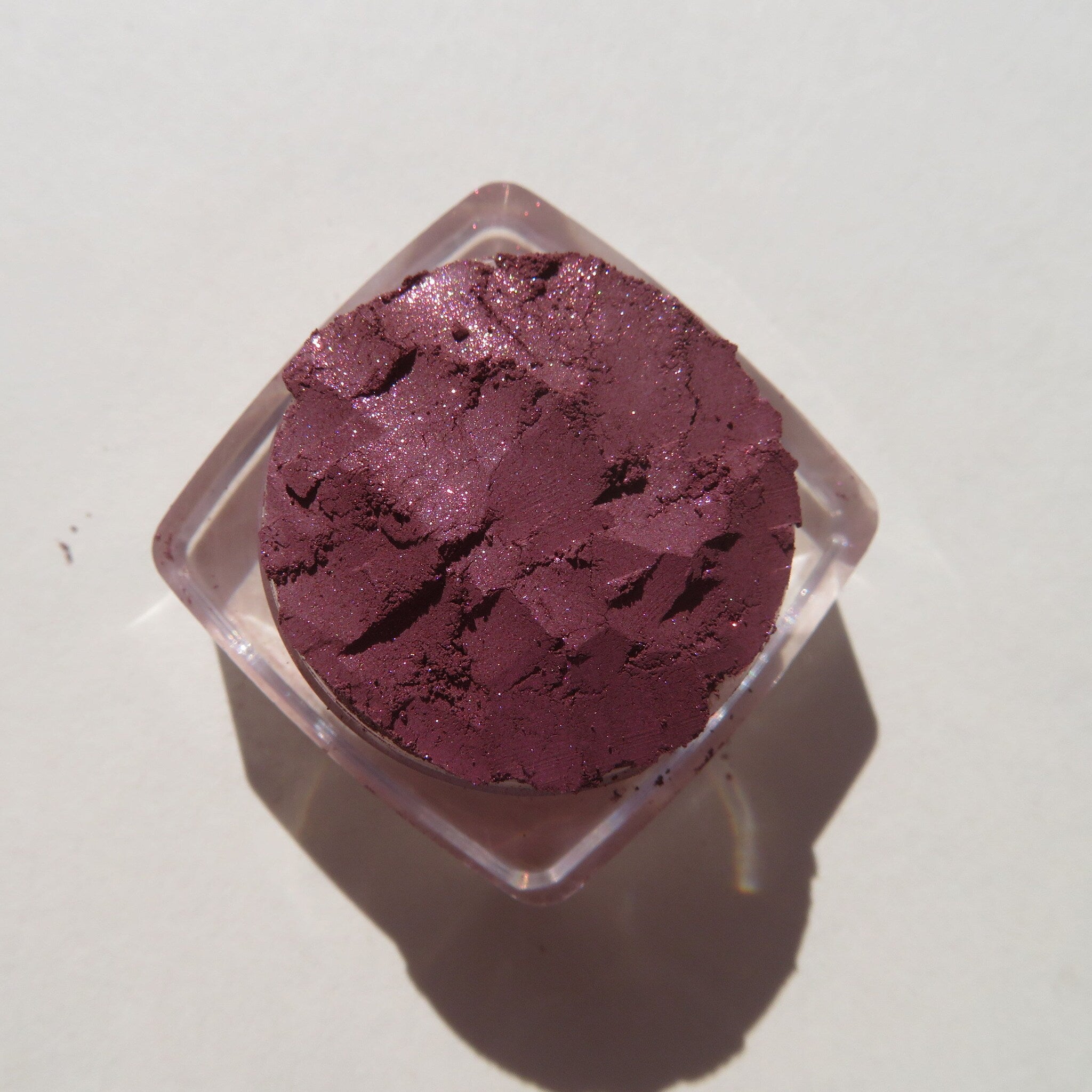 Side view of loose vegan mineral eye shadow in dark mauve with pink sheen, showcasing pigment texture