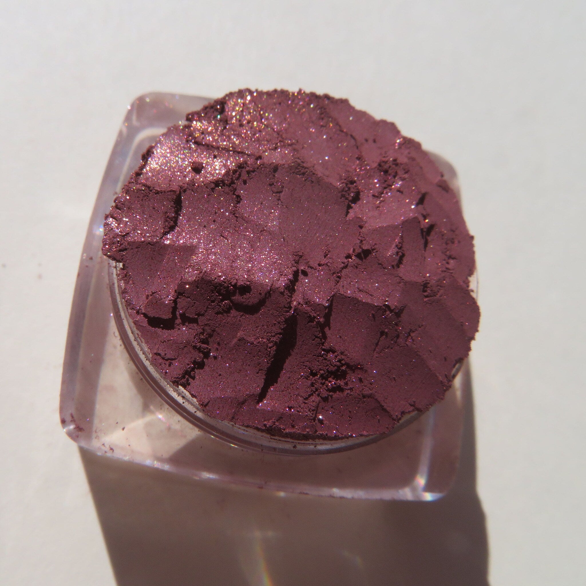 Close-up of loose vegan mineral eye shadow in dark mauve with shimmering pink sheen, cruelty-free pigment.