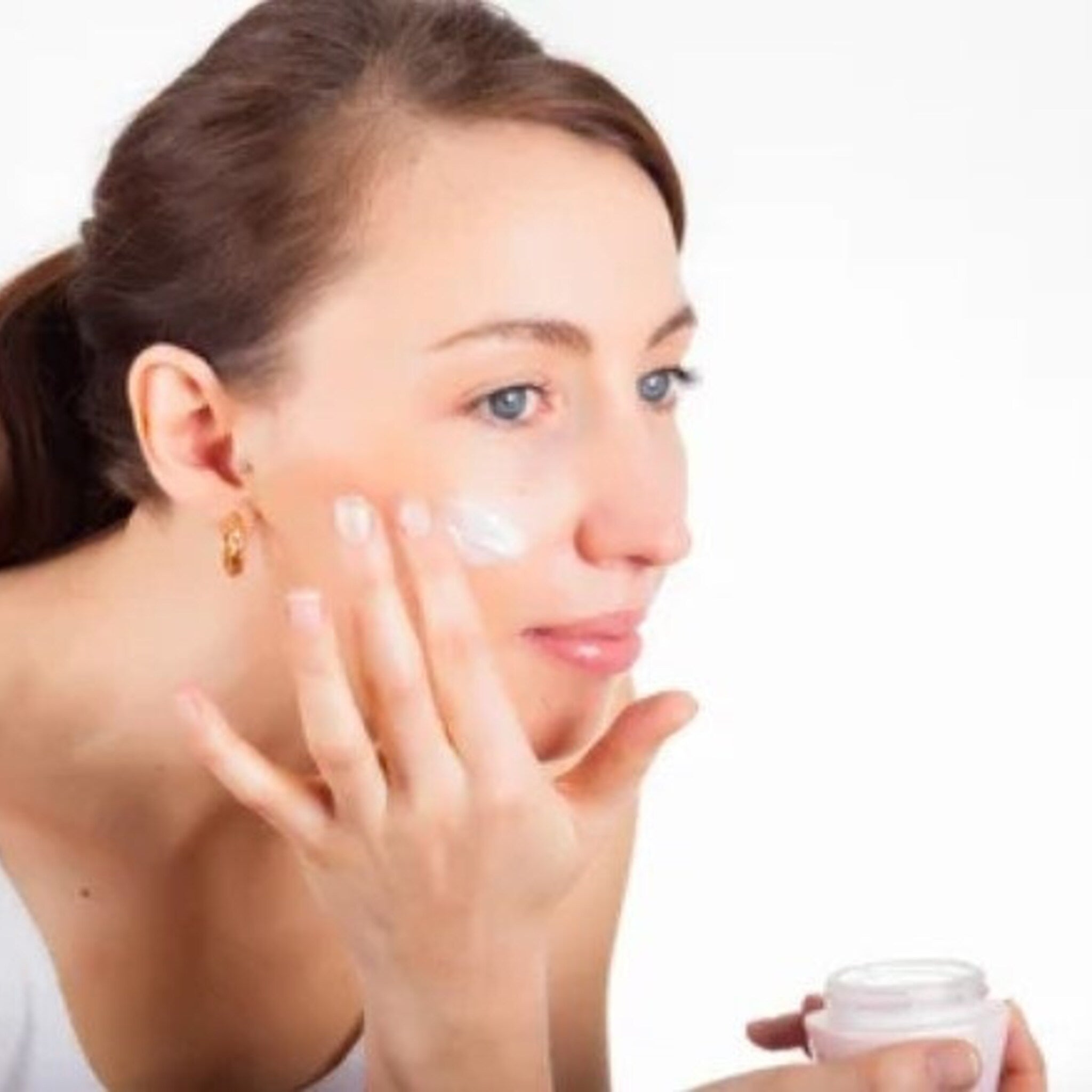 Close-up of creamy white moisturizer with natural extracts in a sleek silver jar, texture shown on fingertips