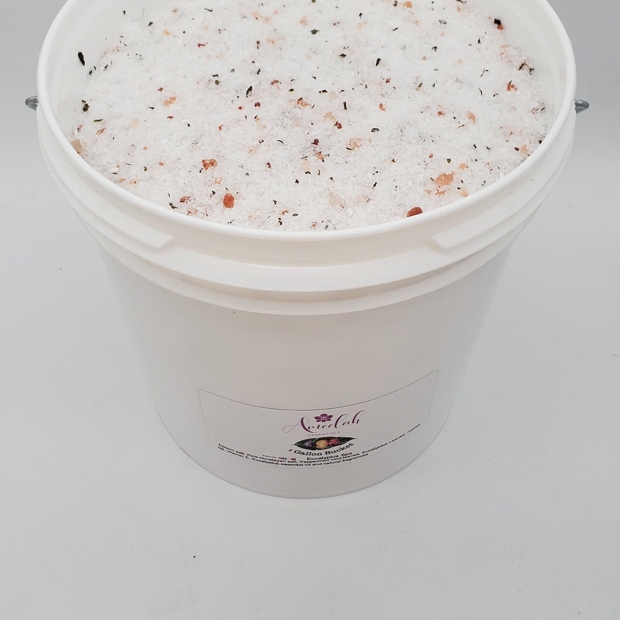 Eucalyptus spa salt with white, pink, and green granules in white bucket, Ameelah Essentials label visible