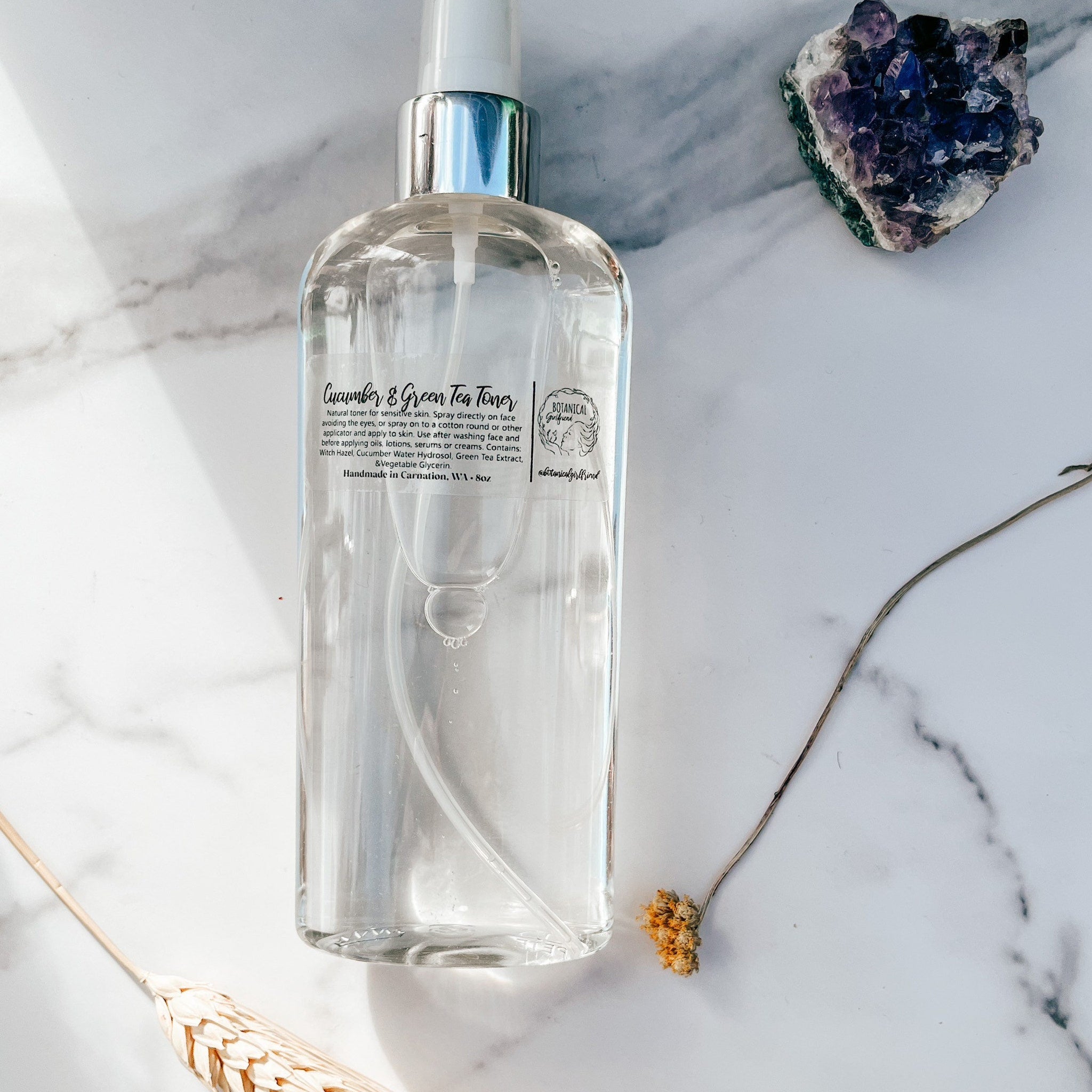 Toner spray bottle, clear liquid, silver cap, Botanical Girlfriend label, on marble surface