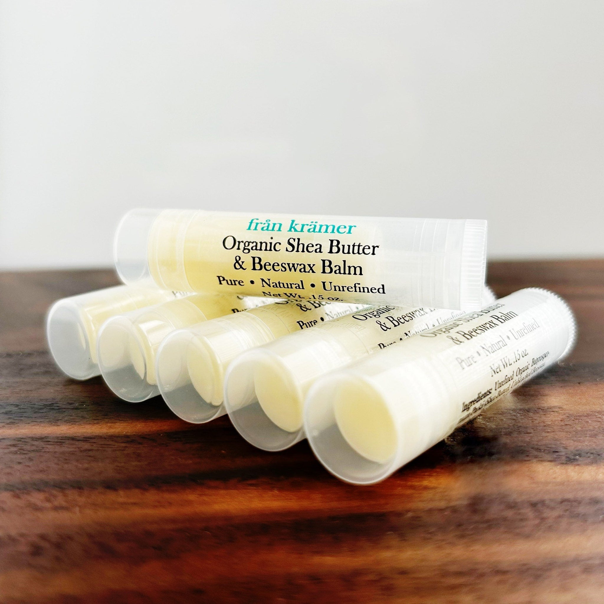 Lip balm tubes in clear plastic, white label with frn krmer text, on wooden surface