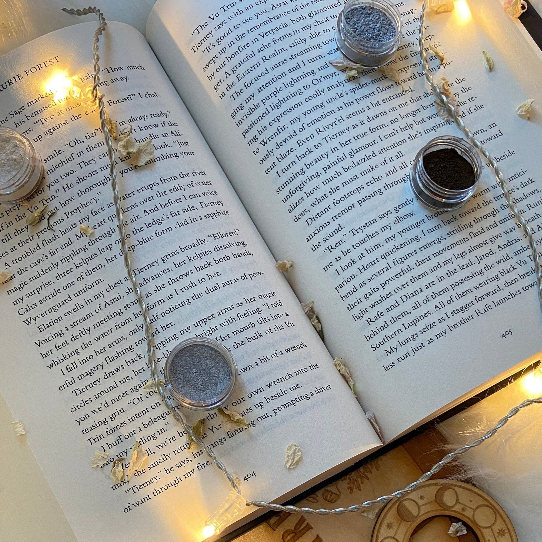 Open book with string lights, small jars of powder, and dried flowers on page