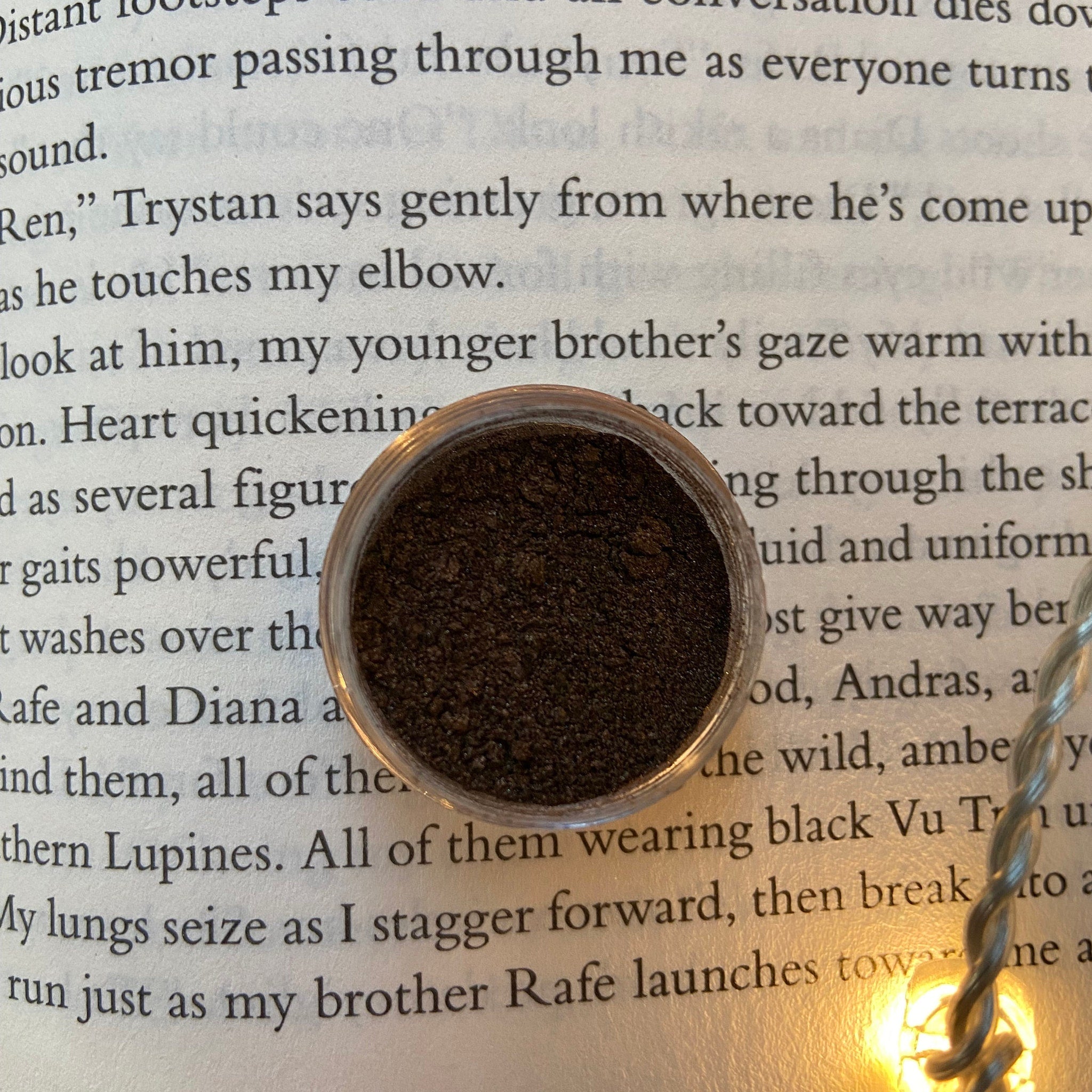 Powdered makeup in a clear jar, dark brown color, sitting on a book page with text
