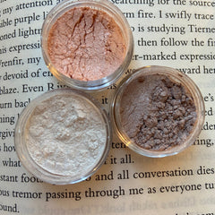 Close-up of a hand applying shimmery taupe eye shadow with a fluffy brush for a blended look