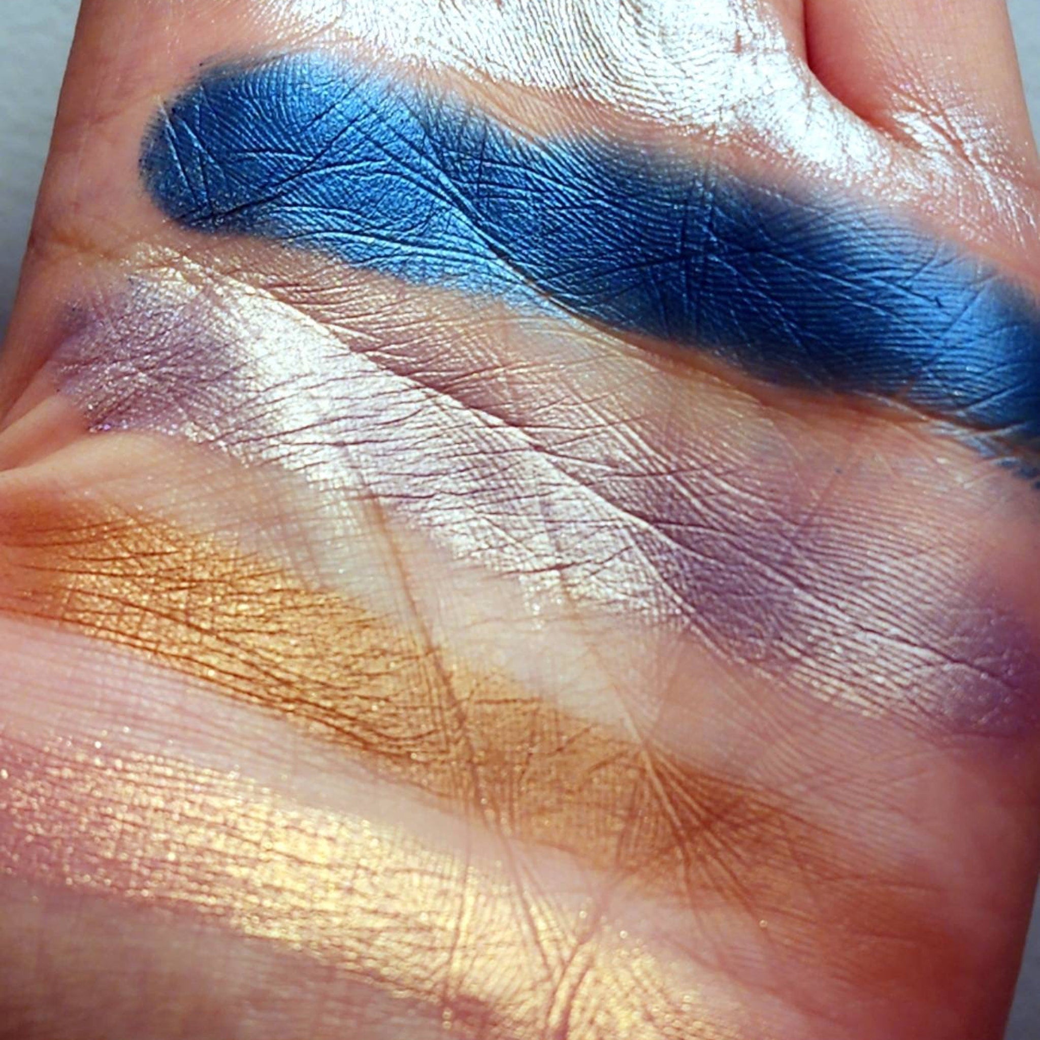 Eyeshadow swatches, metallic blue, gold, and purple shades on skin, textured appearance