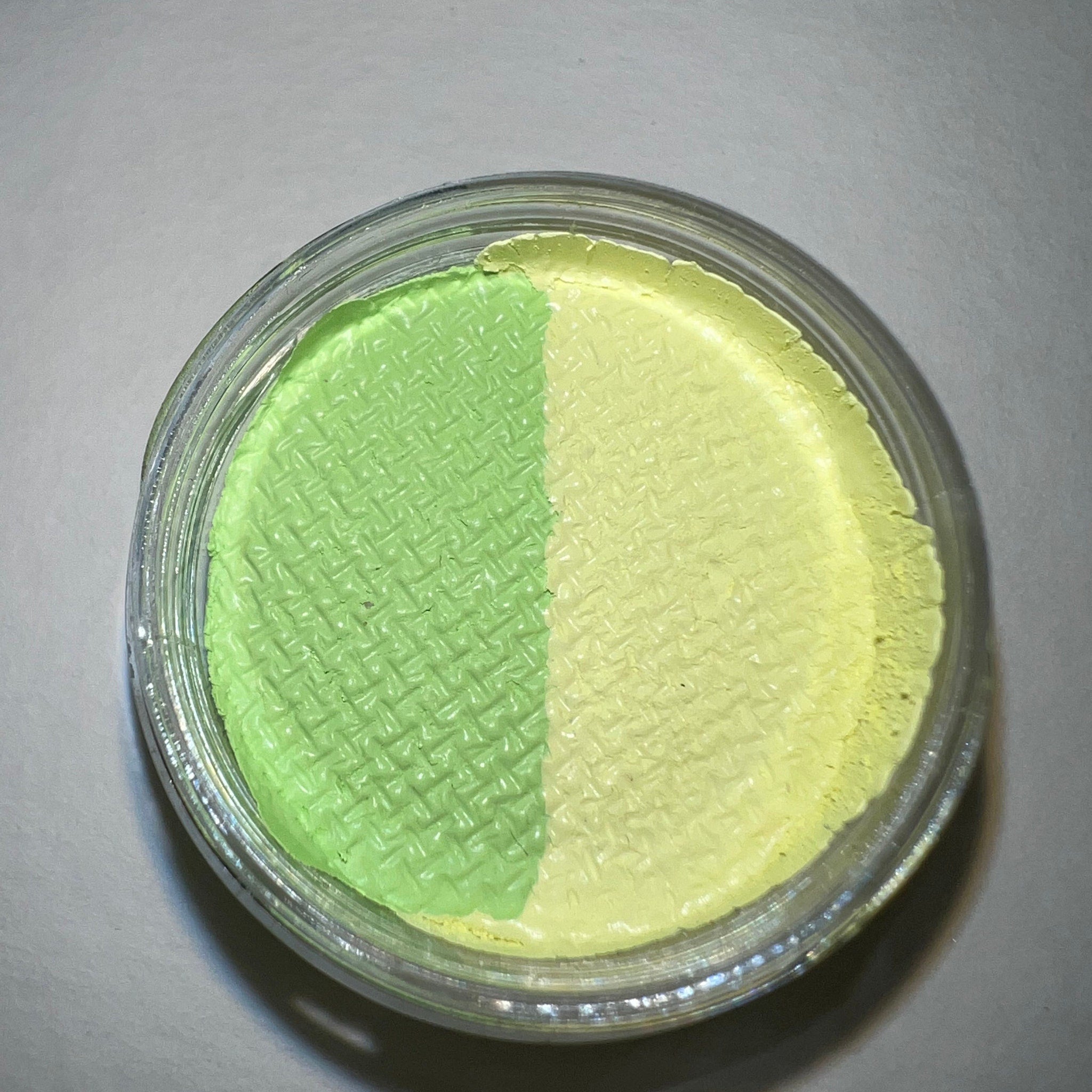 Close-up of vibrant lime green cream eyeshadow with glossy finish in sleek black compact