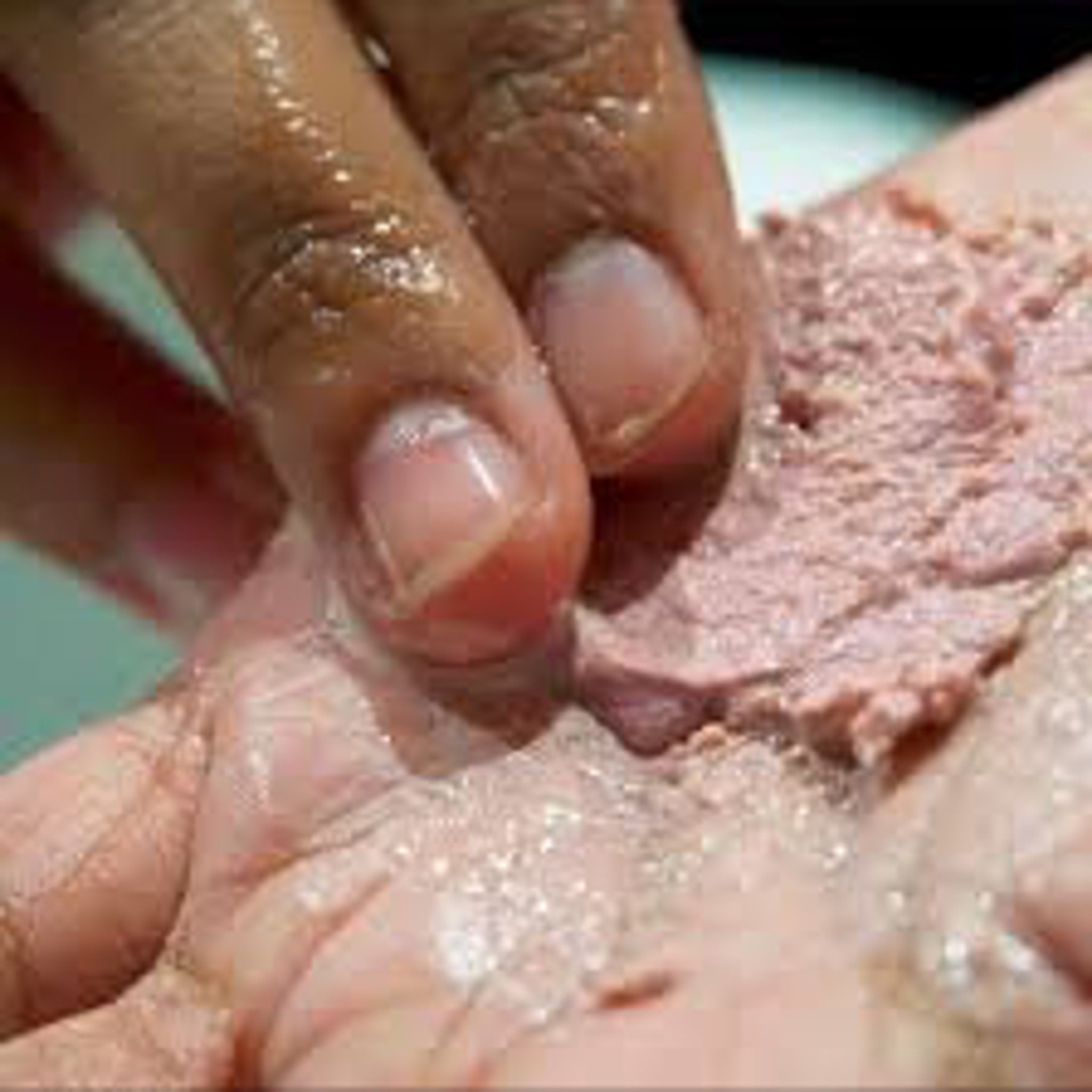 Hand with pink cream and clear liquid, close-up view of application