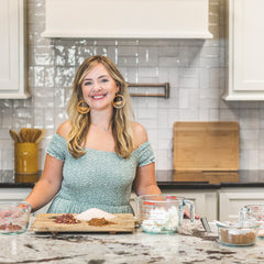 Woman in green floral dress preparing food with ingredients and Pyrex measuring cups on countertop