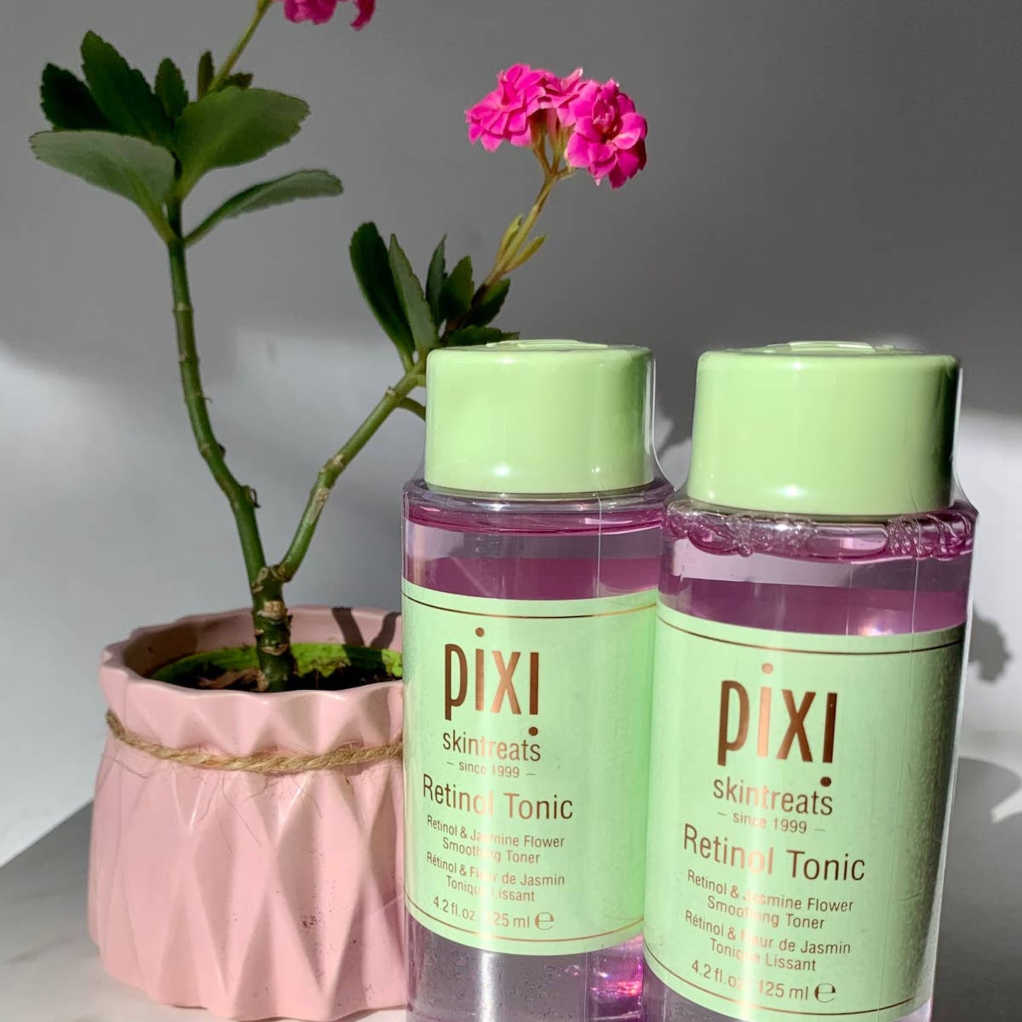 Retinol Toner bottles with green caps and labels, pink liquid, and plant in pink pot with Pixi text