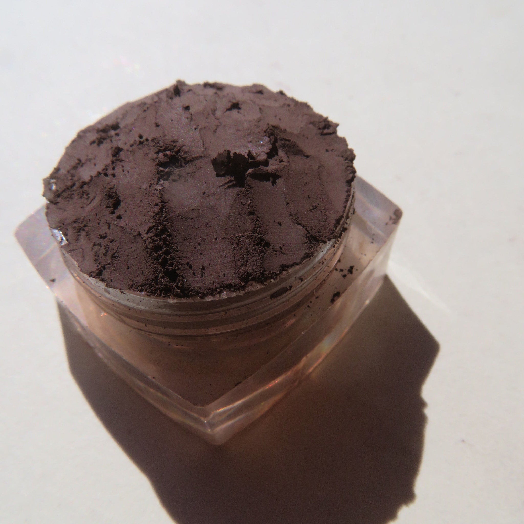 Side view of rich mahogany loose mineral eyeshadow powder in open jar with brush applicator