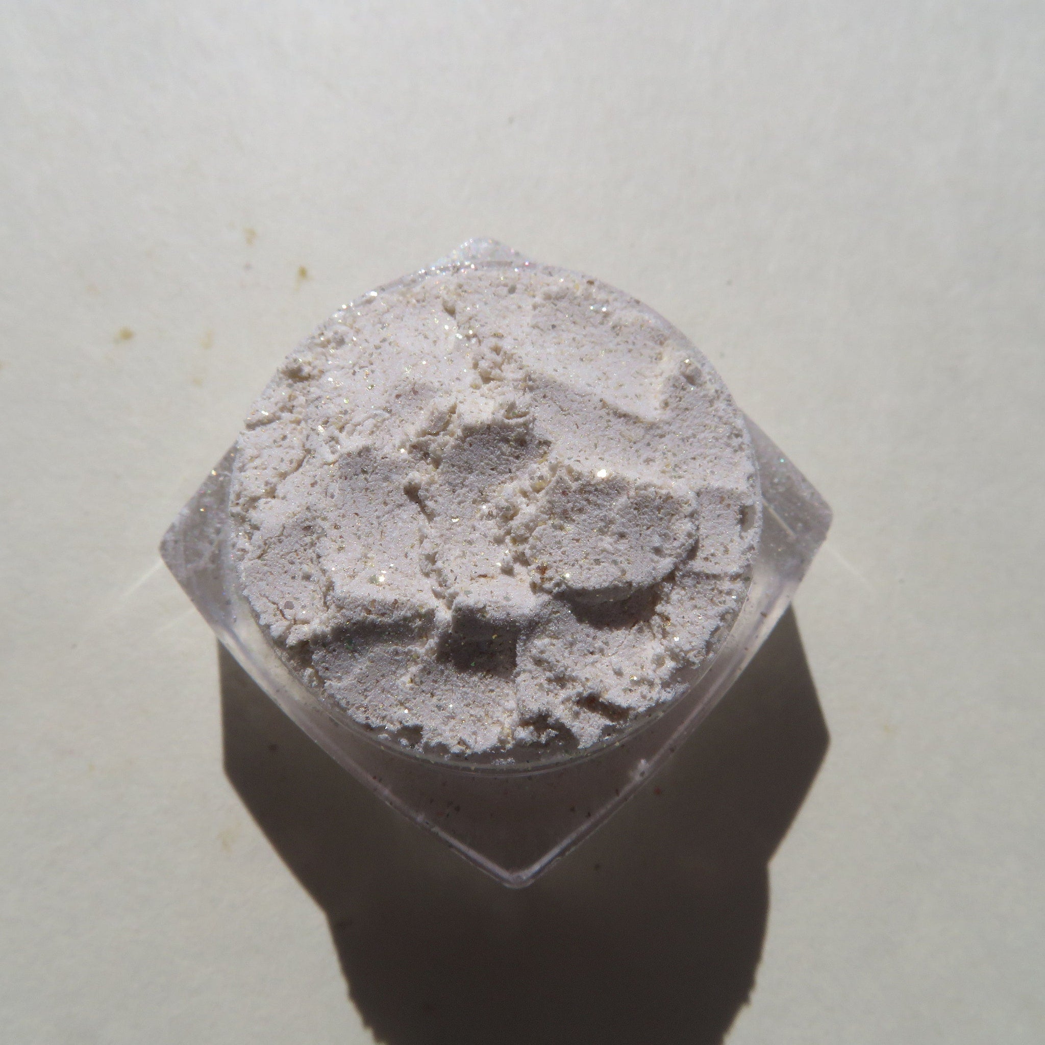 Powdered cosmetic with light beige color, glitter, and clear container
