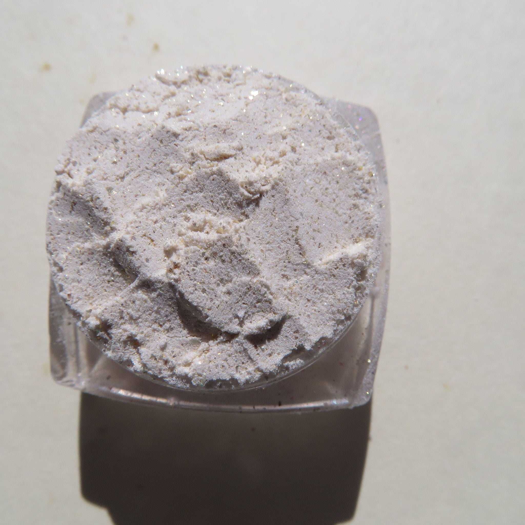 Powdered makeup, off-white with glitter, in a clear plastic container