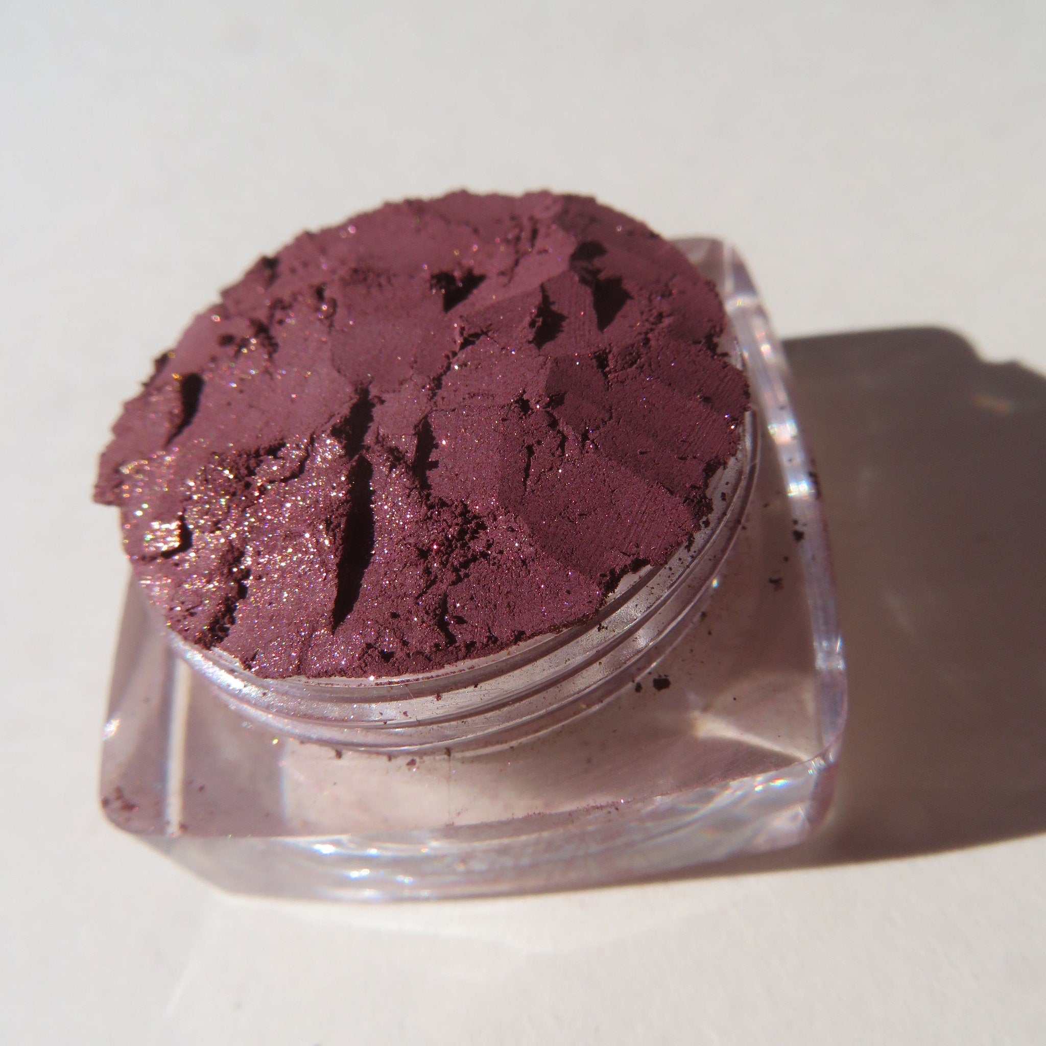 Hand applying loose dark mauve eye shadow with pink sheen using a fluffy brush for a soft blended look.