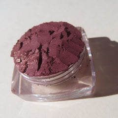 Eyeshadow powder in deep purple with glitter, in a clear plastic container, close-up view
