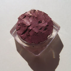 Side view of loose dark mauve eye shadow with pink sheen in minimalist glass jar, showcasing pigment texture
