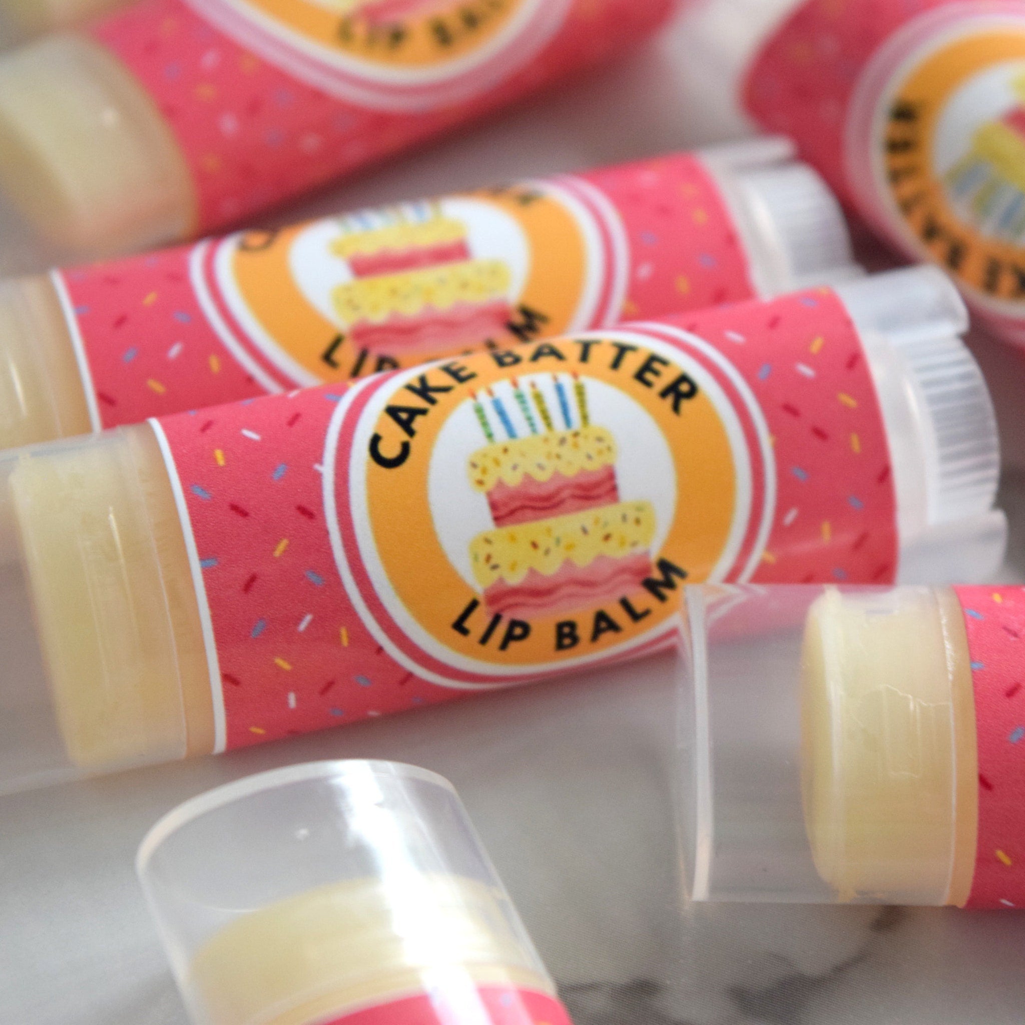 Lip balm tubes with pink confetti pattern, "Cake Batter" label, and clear plastic casing